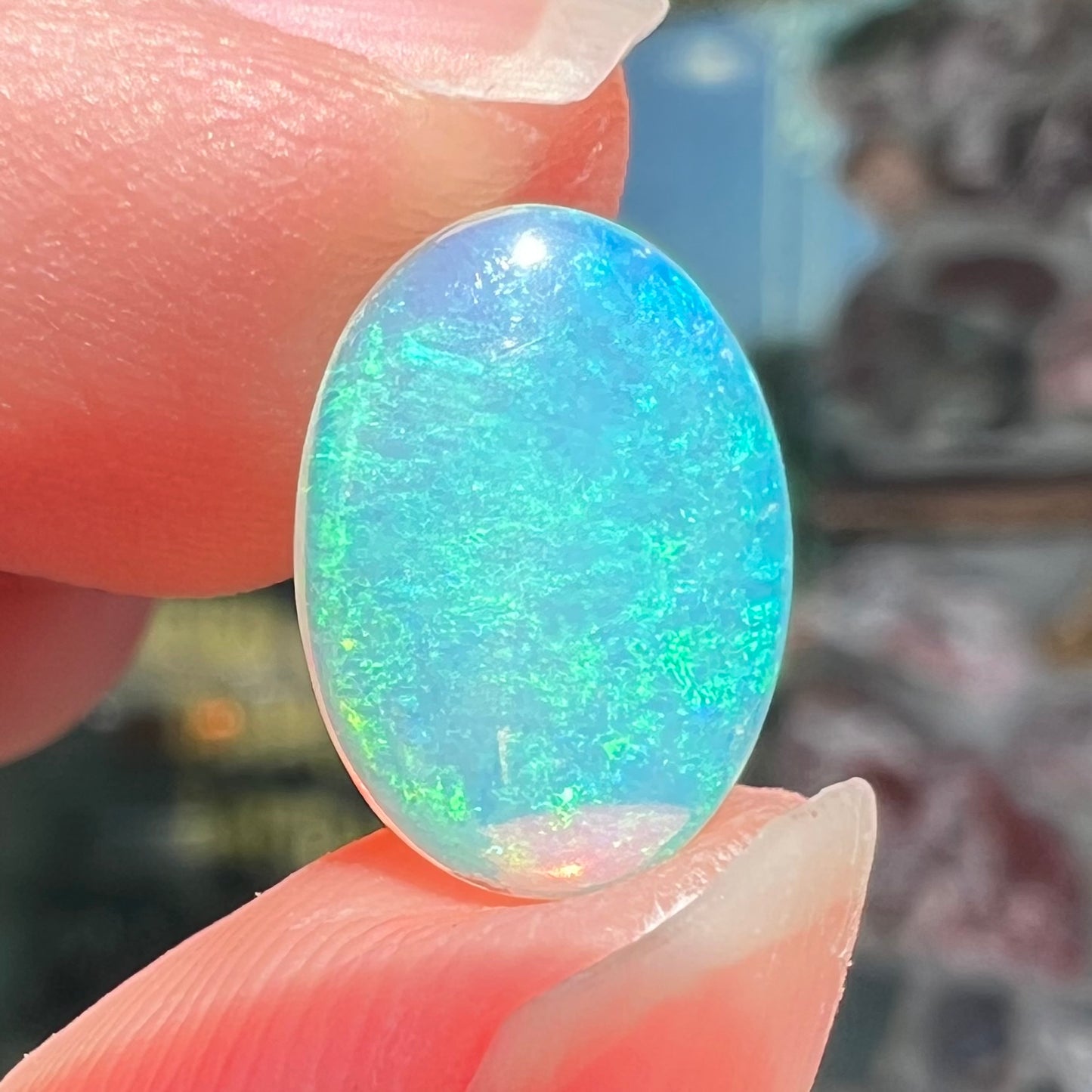 A loose, oval cabochon cut crystal opal from Coober Pedy, Australia. The opal has green and blue colors.