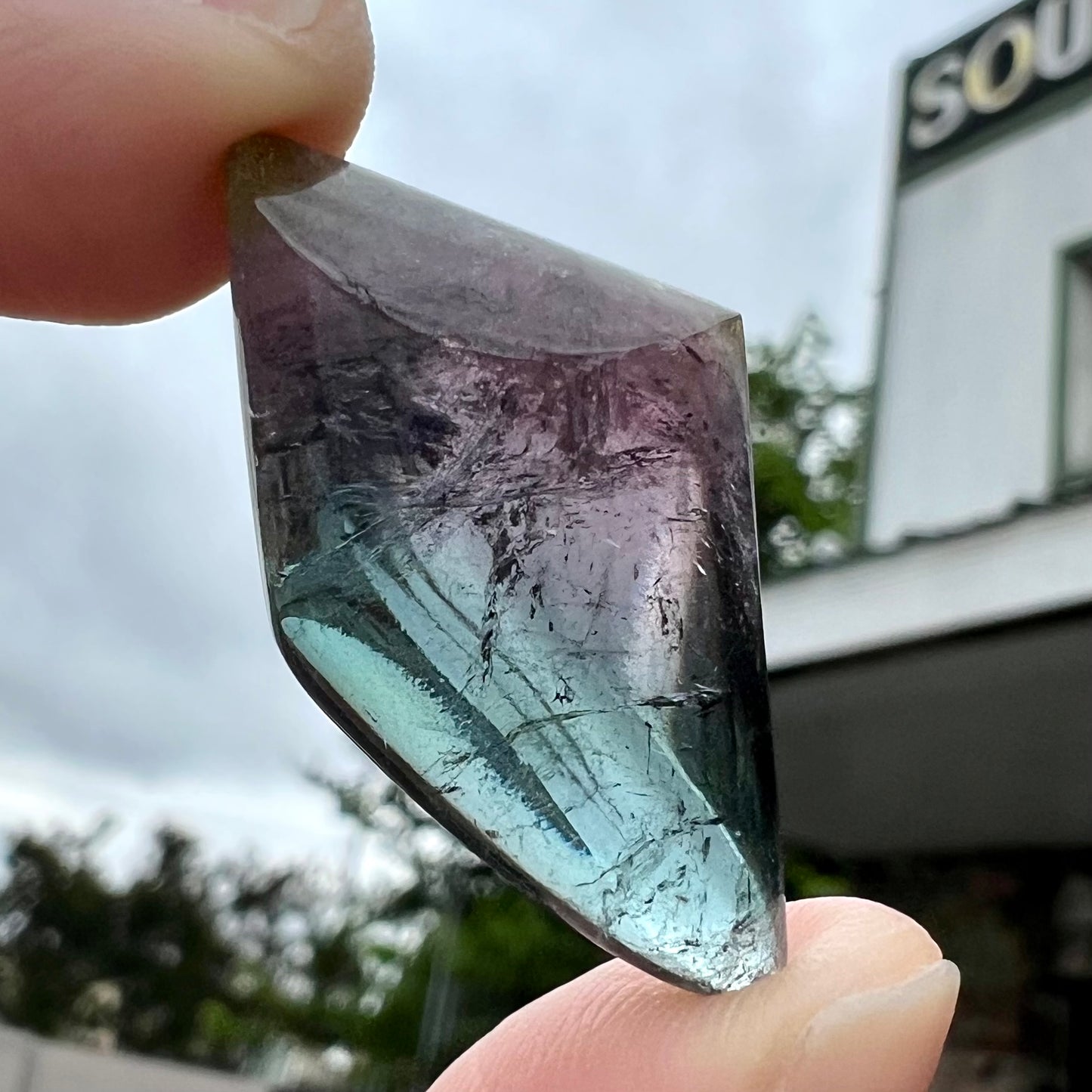 A loose, freeform cabochon cut tricolor tourmaline stone that has blue, pink, and yellow colors.