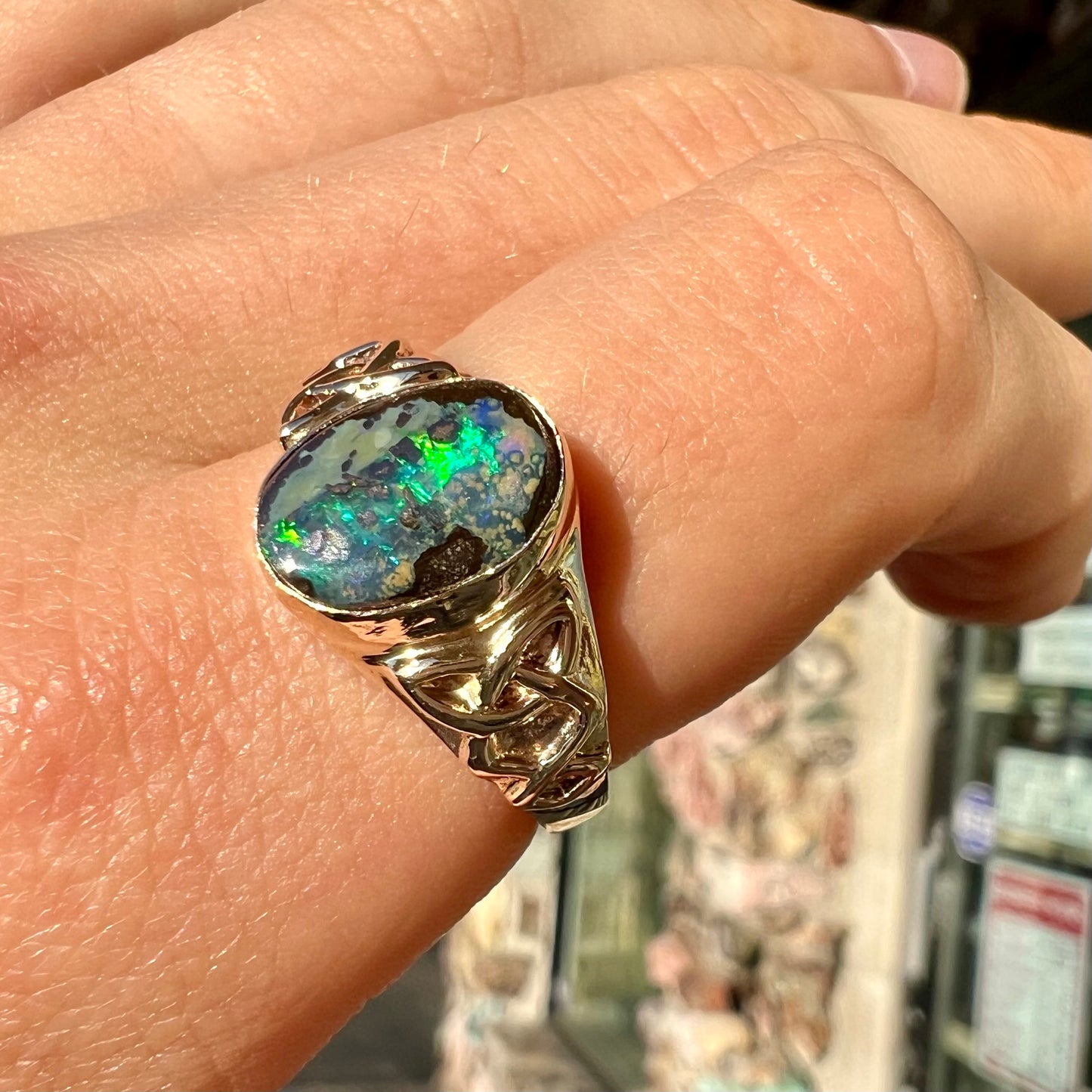 A unisex Celtic style natural boulder opal ring cast in yellow gold. The opal shines green and blue.