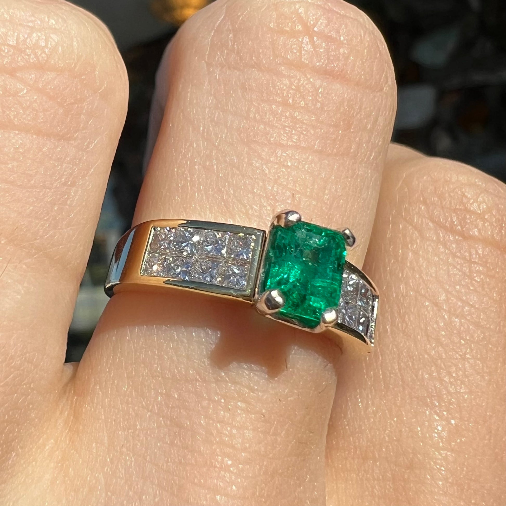 An 18 karat yellow gold ladies' emerald ring, channel set with princess cut diamonds.