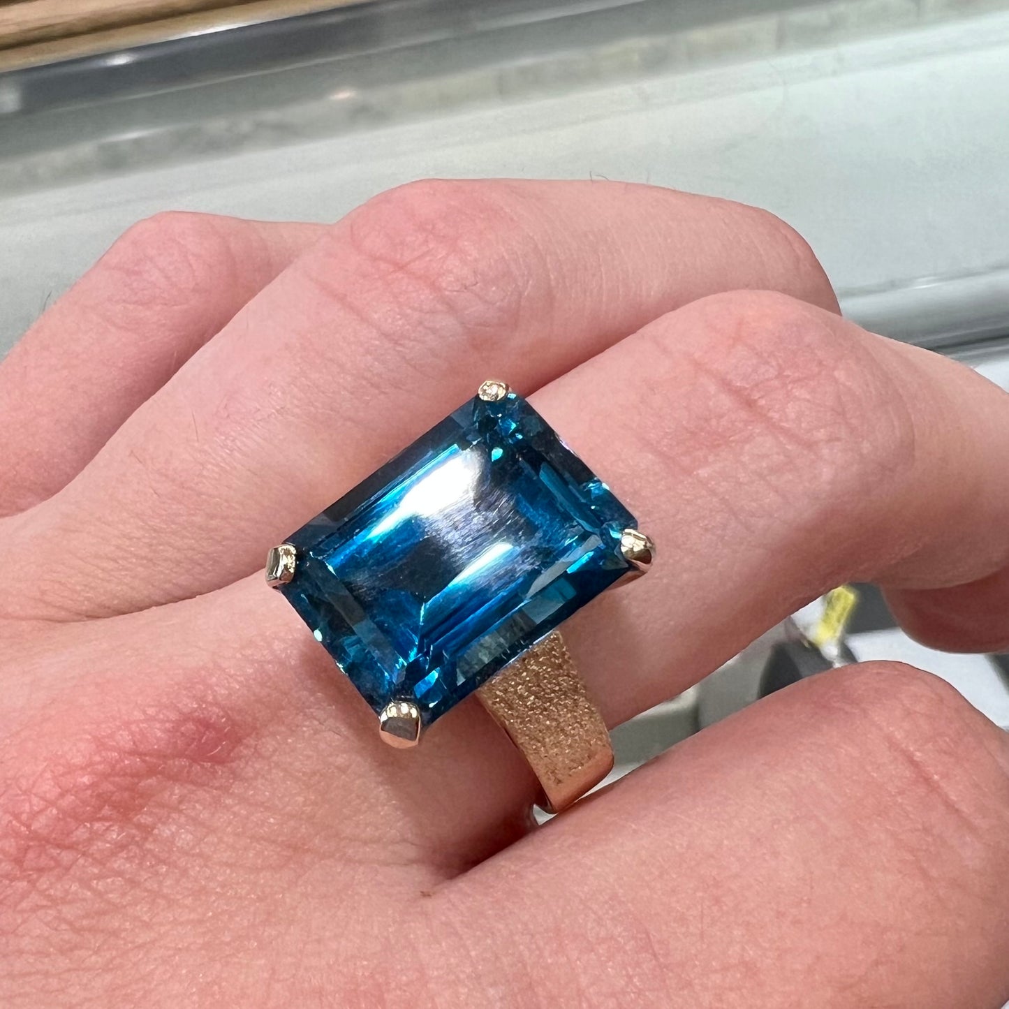 A ladies' yellow gold London blue topaz solitaire ring. The ring is textured, and the topaz is emerald cut.