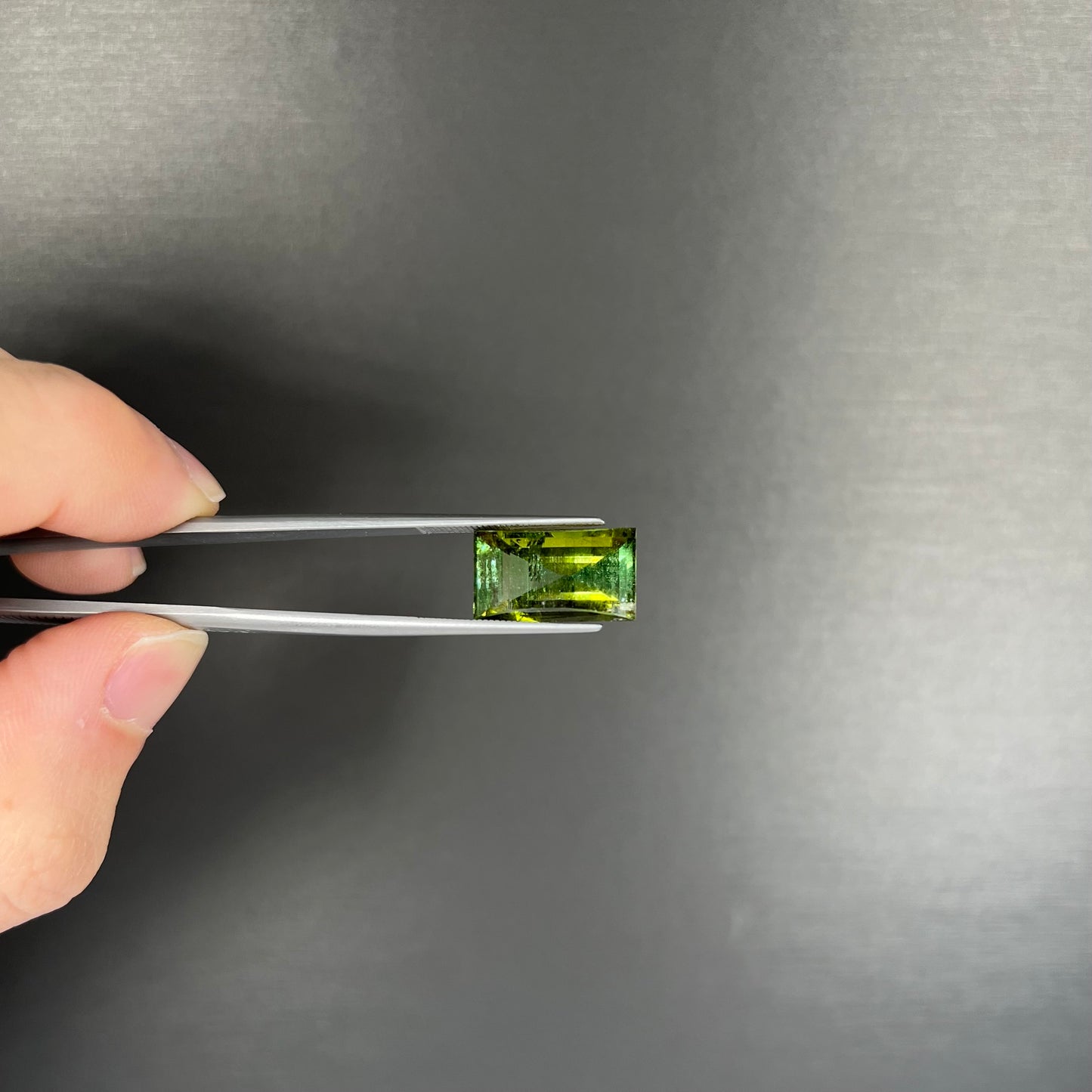A rectangular step-cut yellowish green tourmaline gemstone.