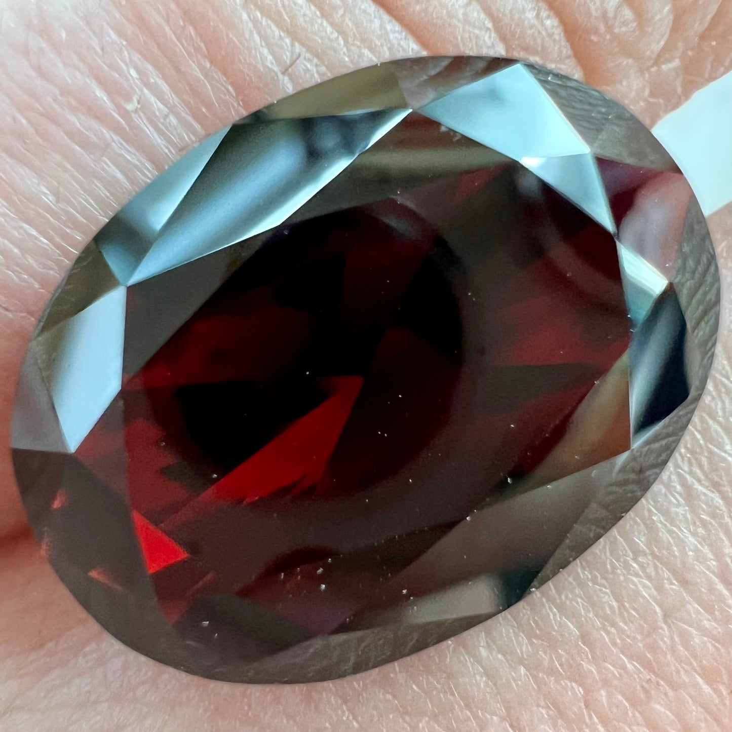 A loose, faceted oval cut pyrope garnet gemstone. The stone is a deep, dark red color.