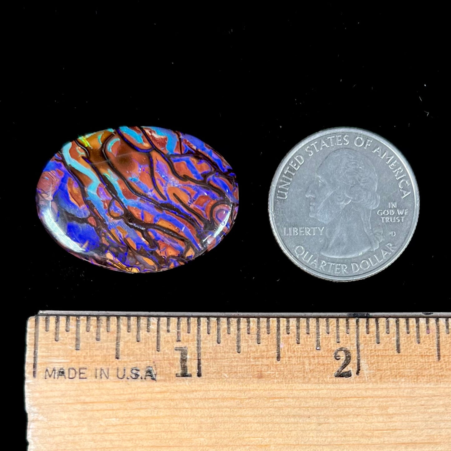 A loose, oval cabochon cut boulder opal from Koroit, Australia. The opal has violet and purple veins.