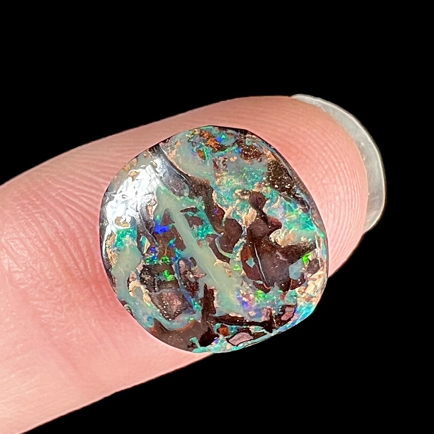 An off-round cabochon cut boulder opal stone from Koroit, Australia. The opal has green, blue, and red colors.