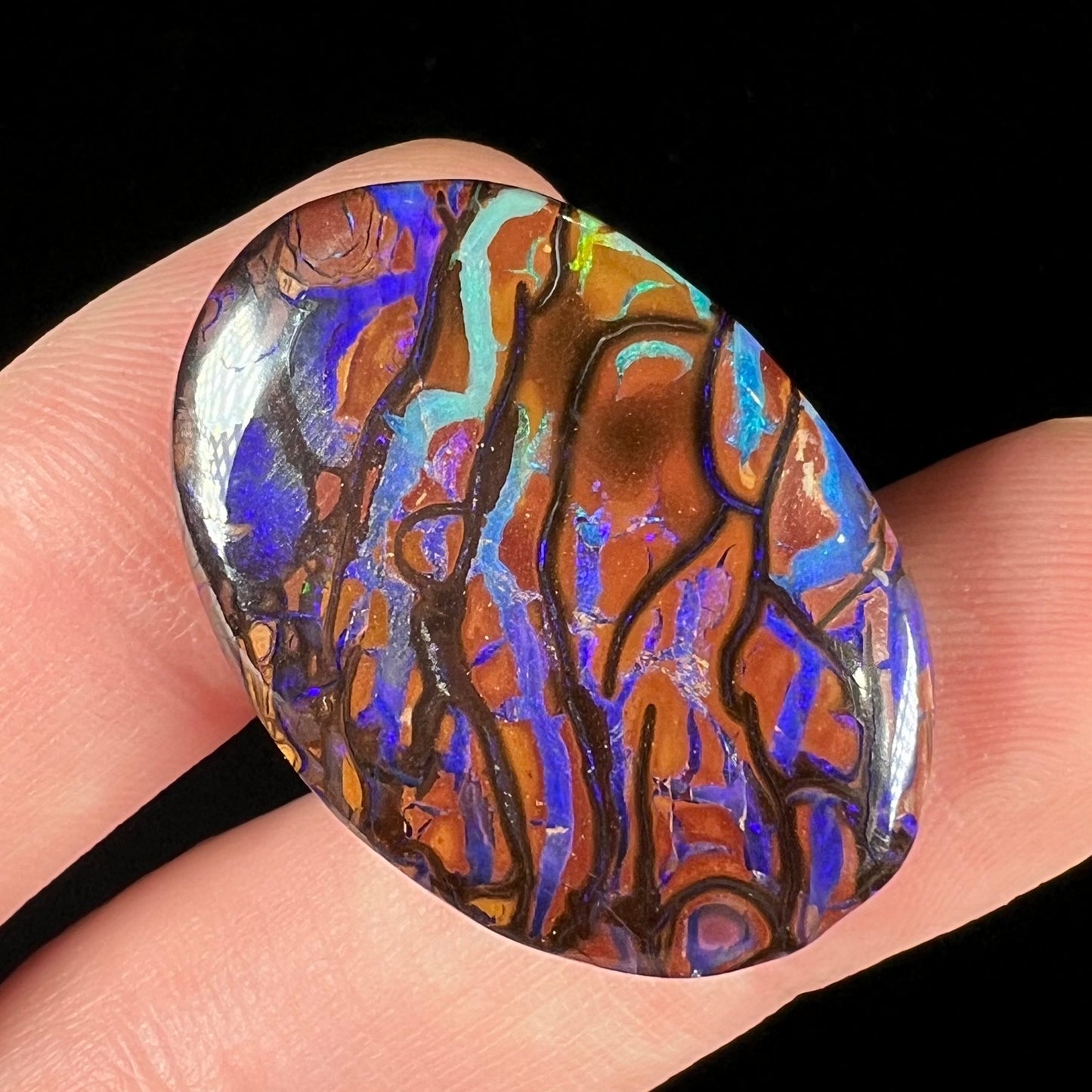 A loose, oval cabochon cut boulder opal from Koroit, Australia. The opal has violet and purple veins.