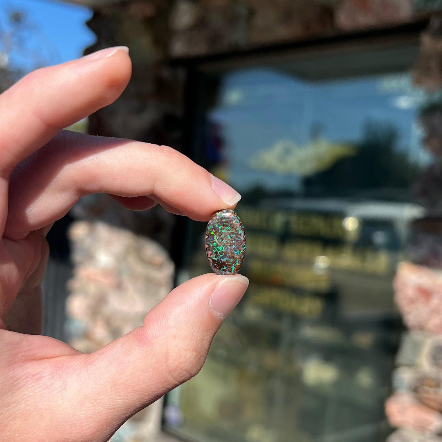 A loose, oval cabochon cut Koroit boulder opal stone. The opal has green and blue veins.