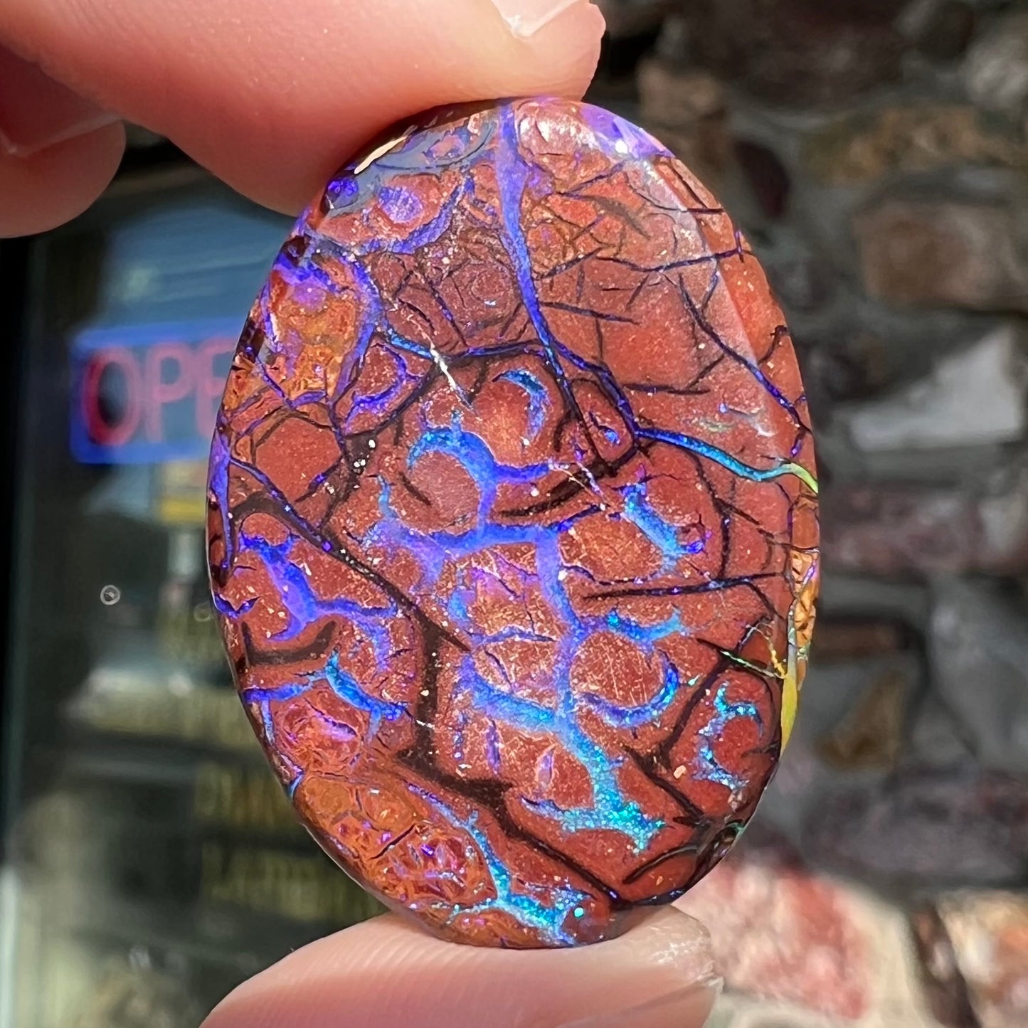 A loose, oval cabochon cut boulder opal from Koroit, Australia. The opal has violet and purple veins.
