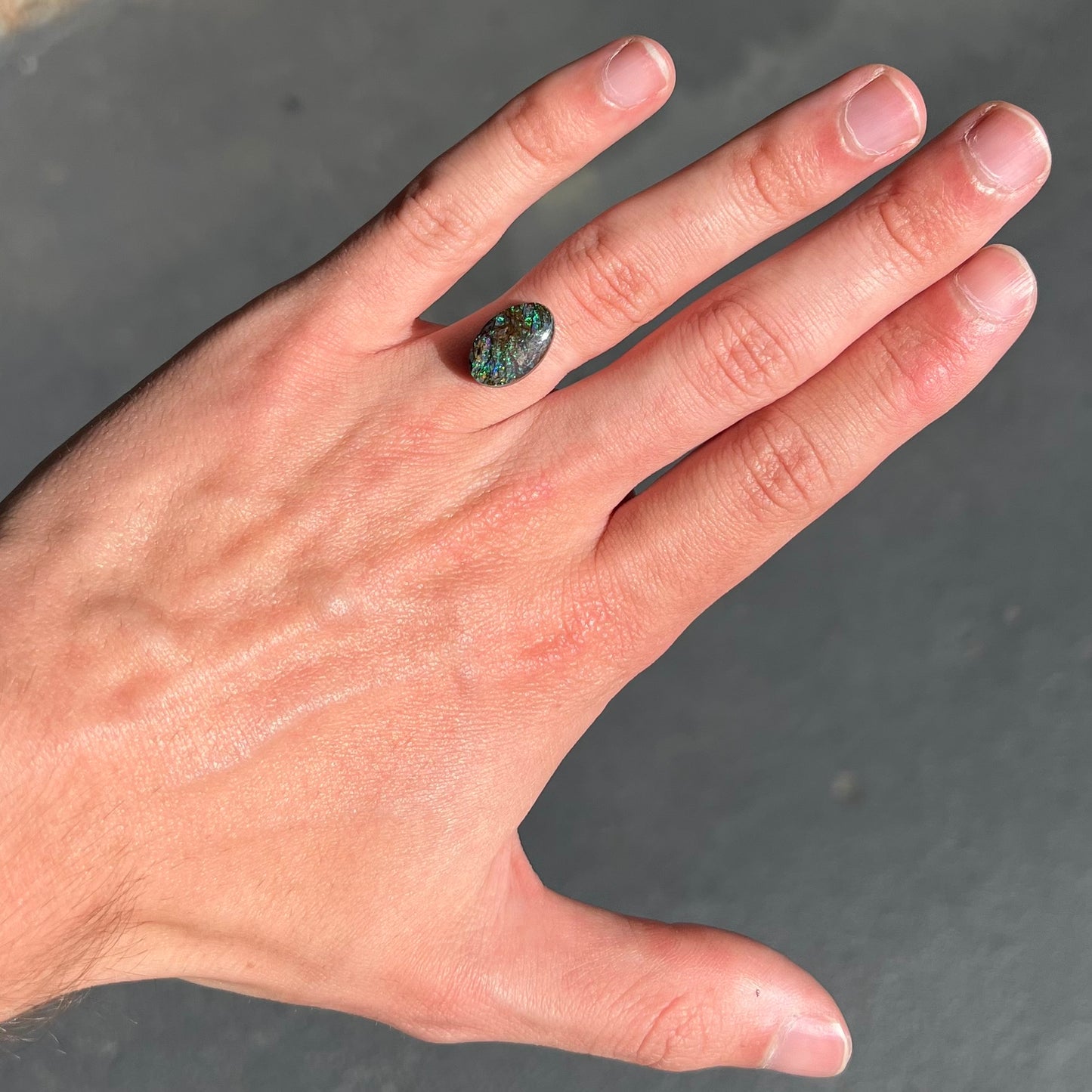 A loose, oval cabochon cut matrix boulder opal stone from Koroit, Australia. The opal shines with green and blue colors.