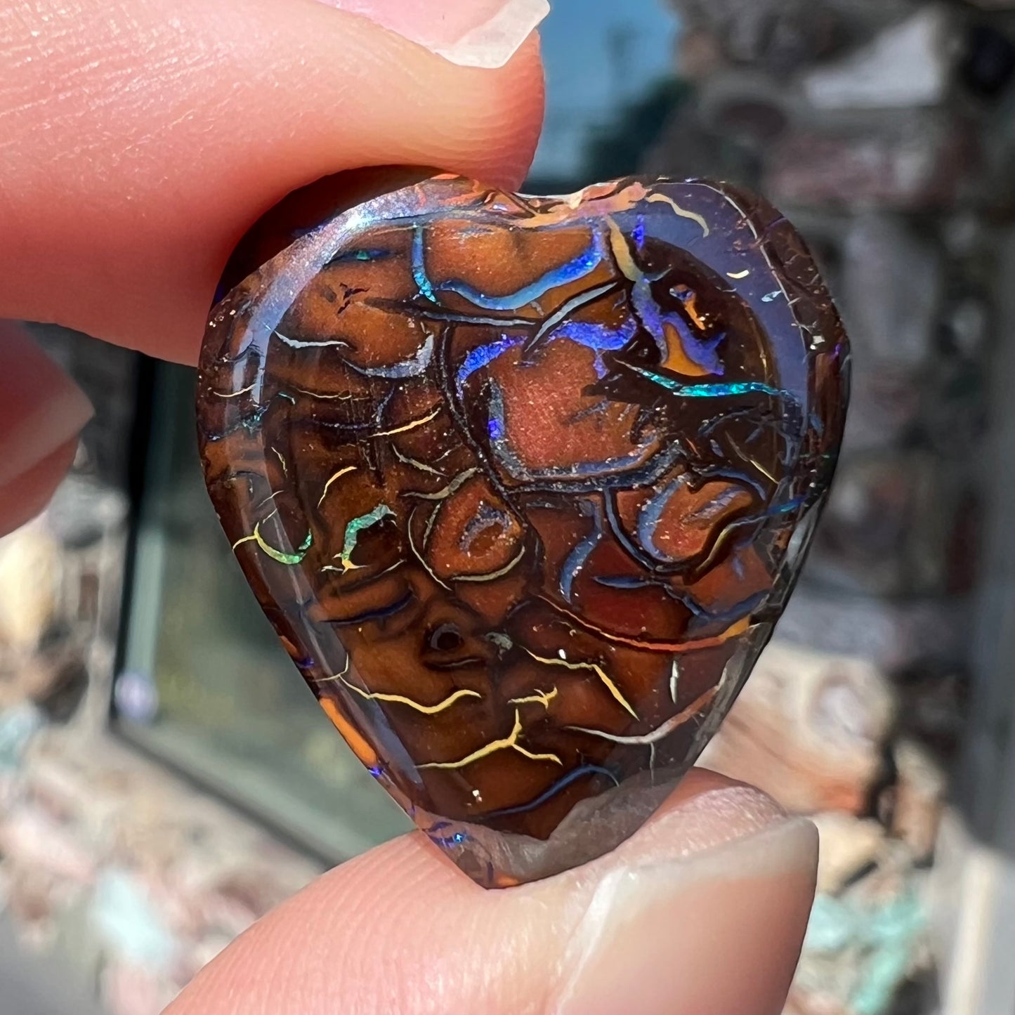 The back of a heart shaped boulder opal stone with purple veins.