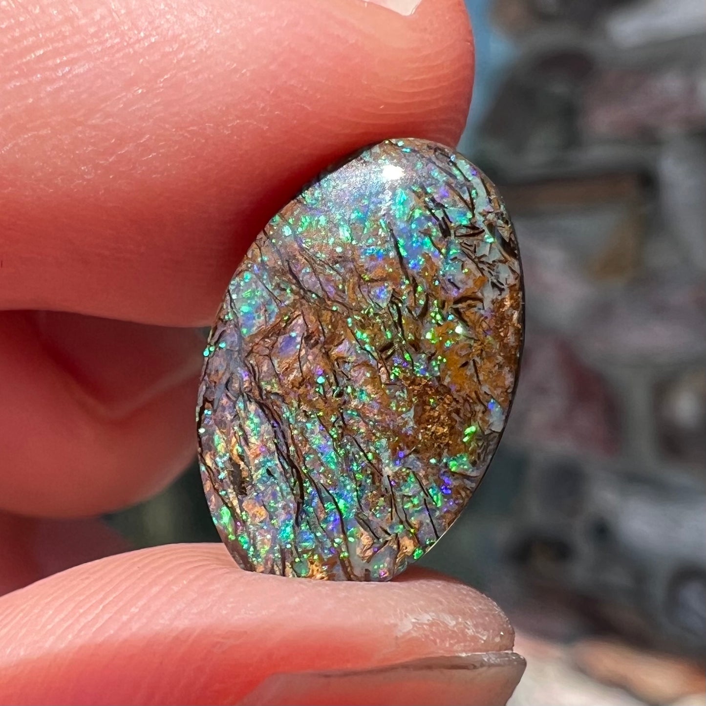 A loose, oval cabochon cut matrix boulder opal stone from Koroit, Australia. The opal shines with green and blue colors.