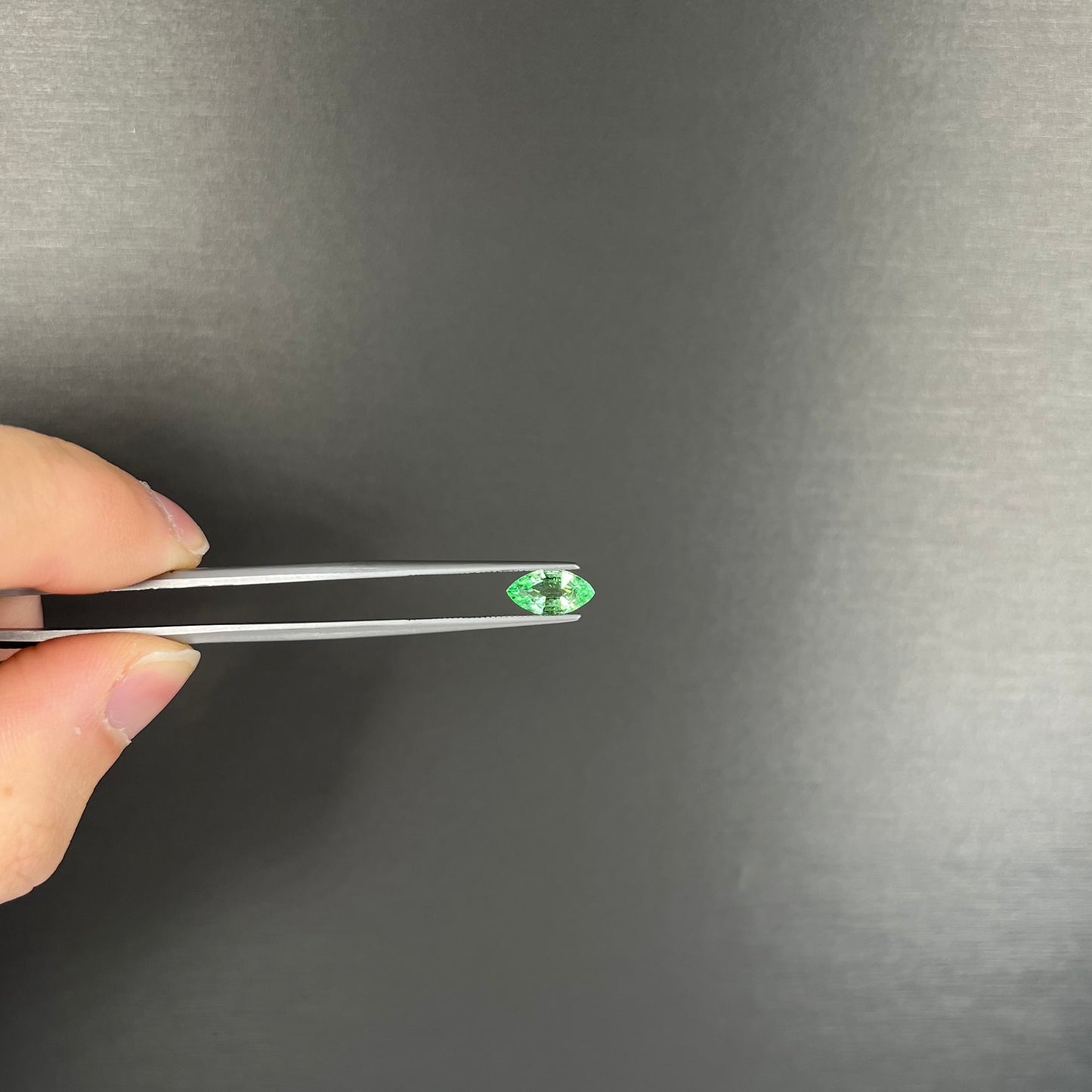 A faceted marquise cut electric green tourmaline gemstone. The stone has an eye-visible rutile needle inclusion.