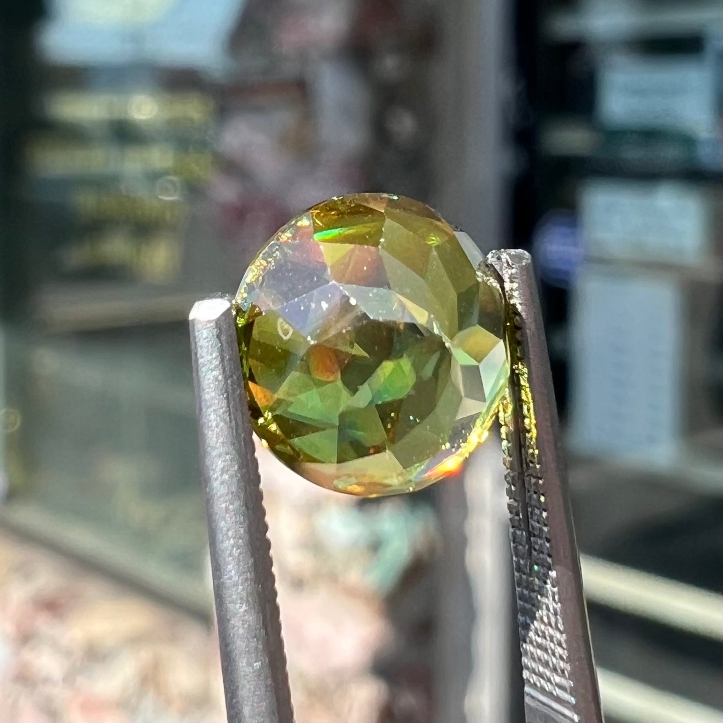 A loose, round brilliant cut sphene gemstone. The stone is green with orange, green, blue, and yellow flashes.