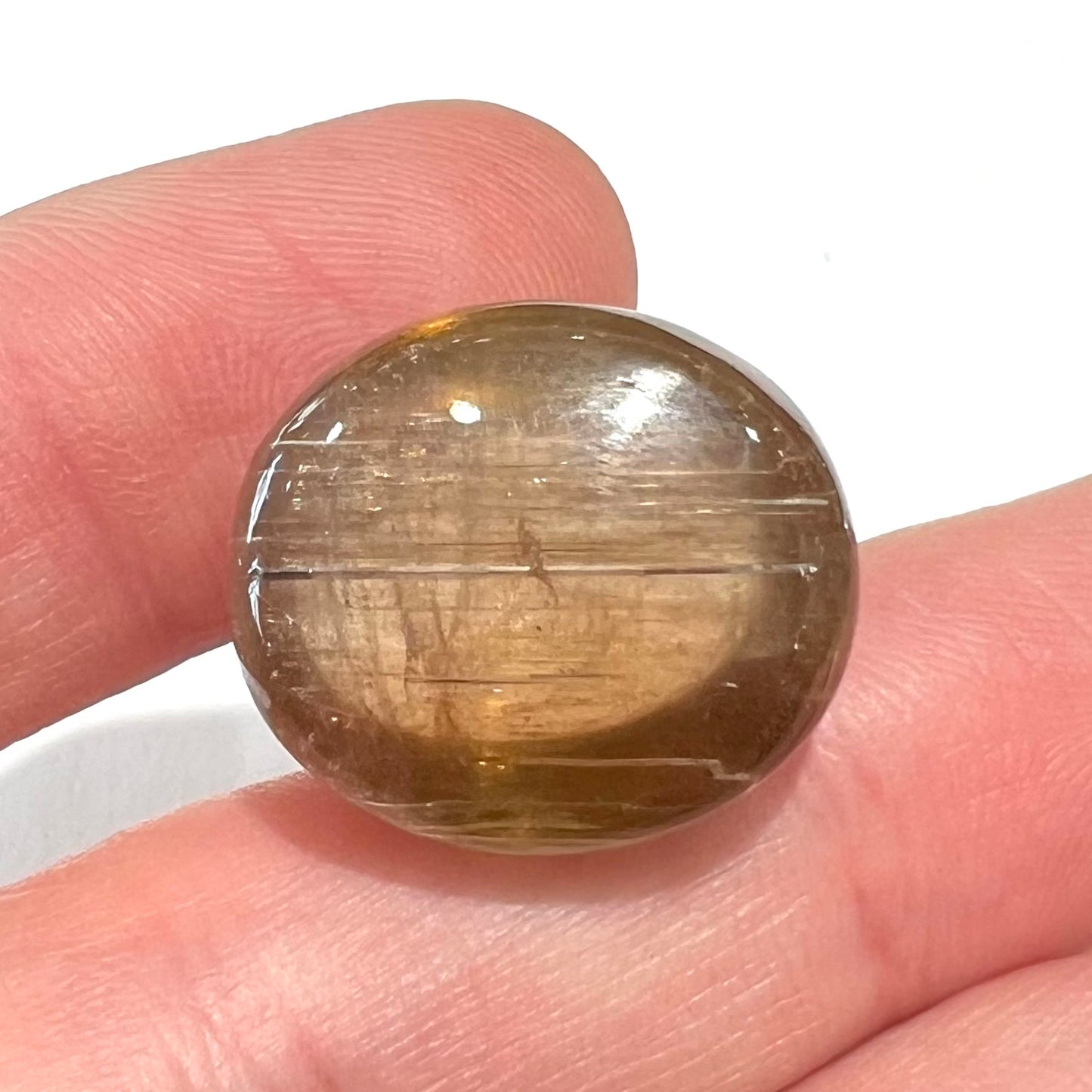 A loose, golden brown cat's eye dravite tourmaline gemstone. The stone is cut into an oval shaped cabochon.