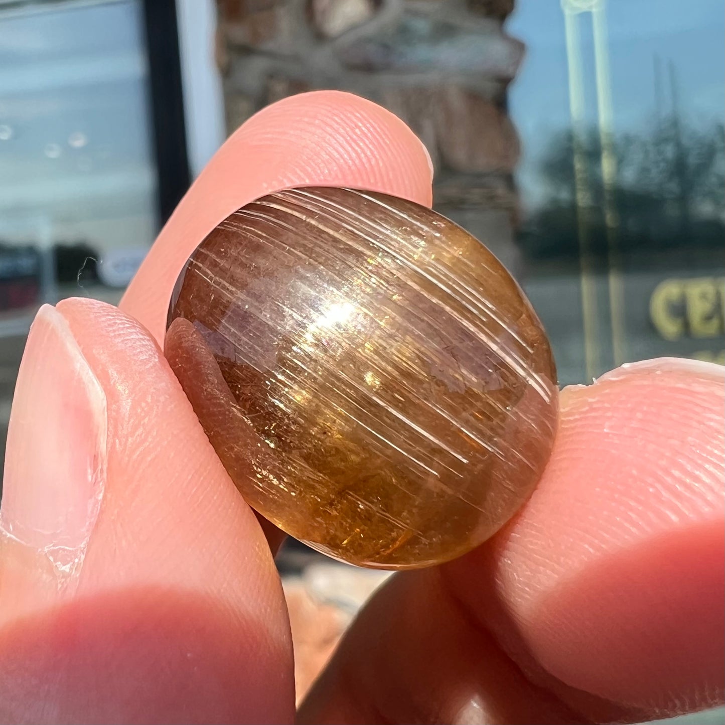 A loose, golden brown cat's eye dravite tourmaline gemstone. The stone is cut into an oval shaped cabochon.
