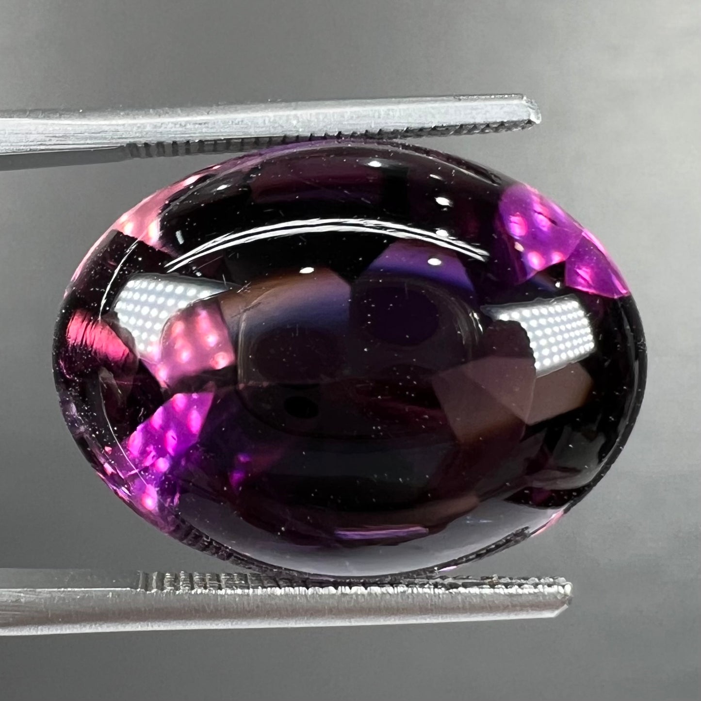 A loose, oval buff top cut amethyst gemstone. The top of the stone is domed, and the bottom is faceted.