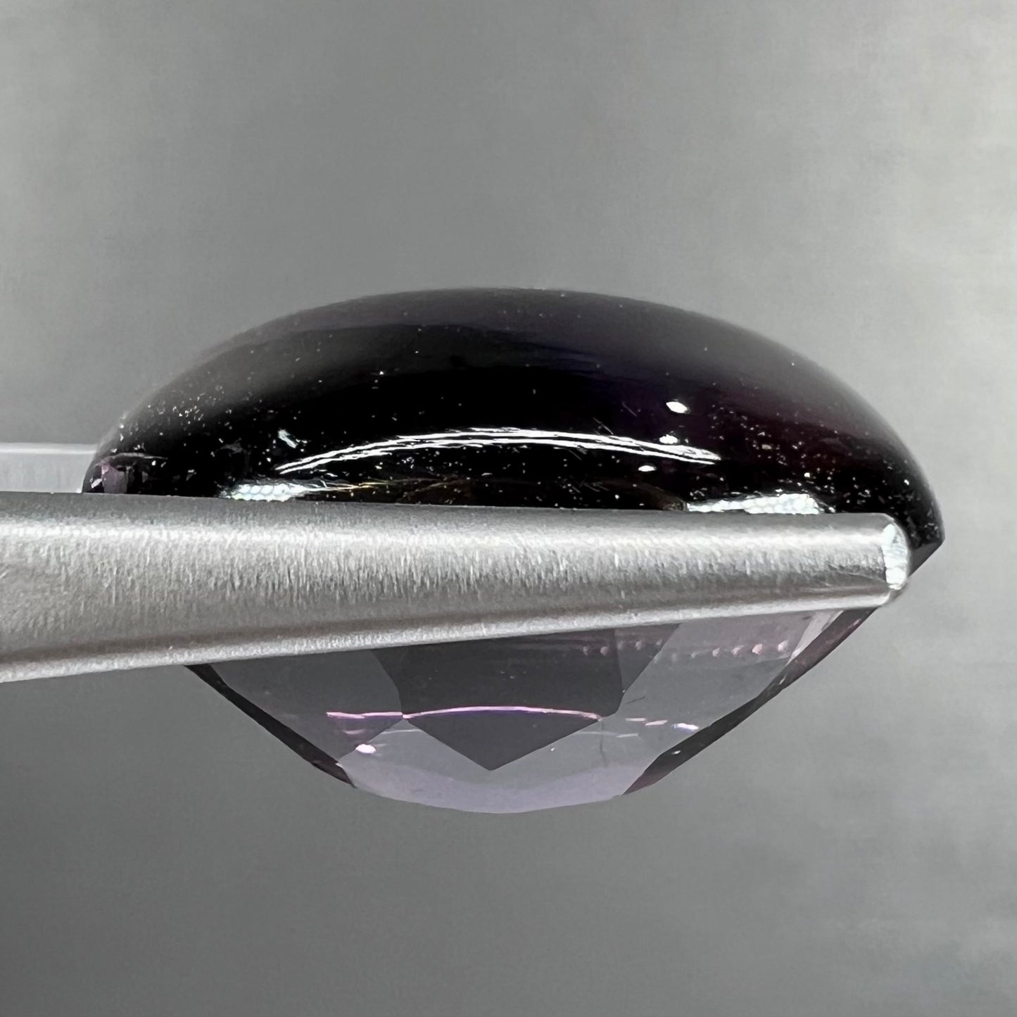 A loose, oval buff top cut amethyst gemstone. The top of the stone is domed, and the bottom is faceted.