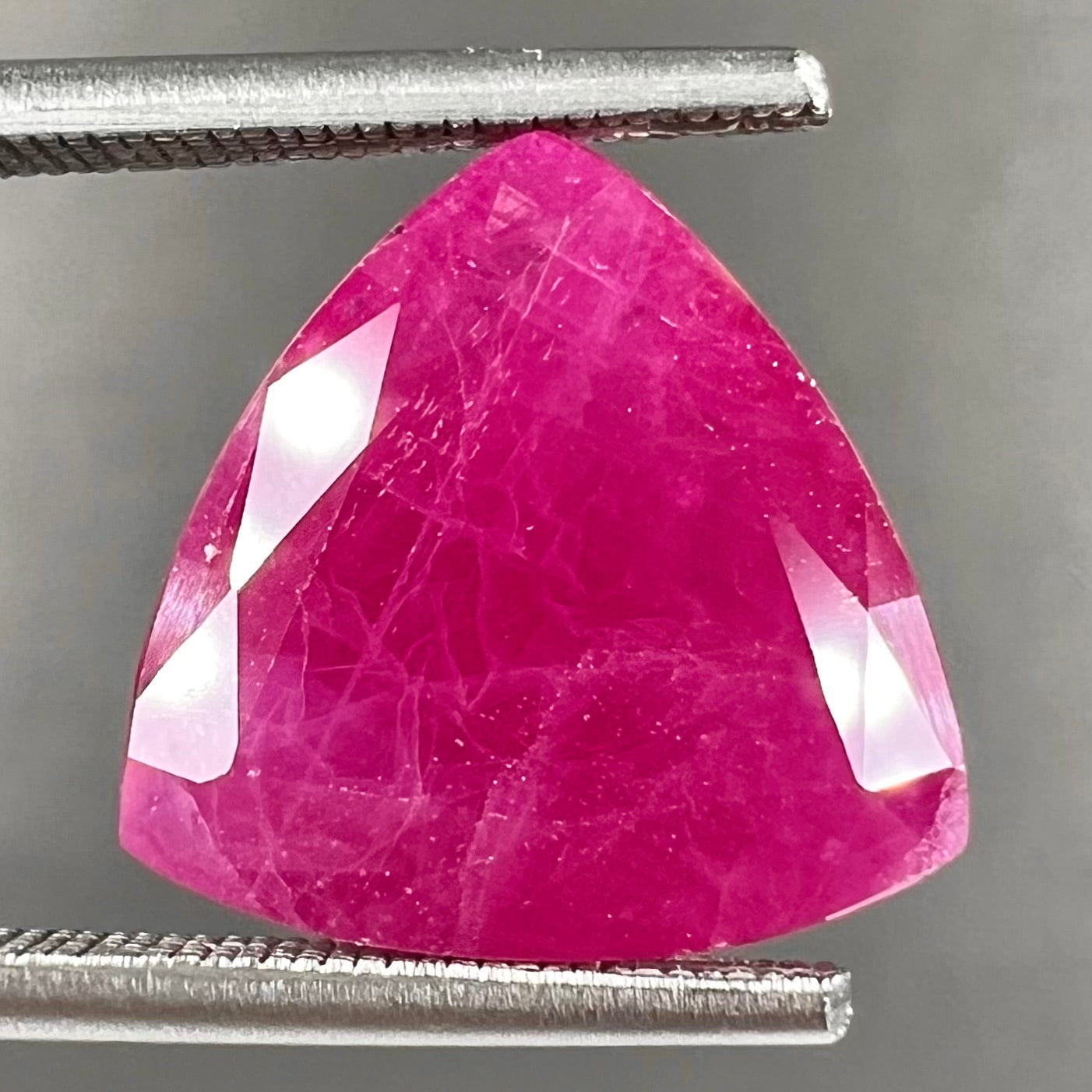 A loose, faceted trillion cut, natural, commercial grade ruby gemstone. The stone is purplish red color.