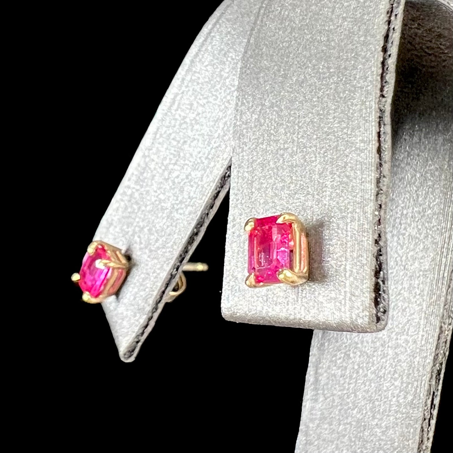 A pair of yellow gold stud earrings set with pinkish red Burmese rubies. The rubies are emerald cut.