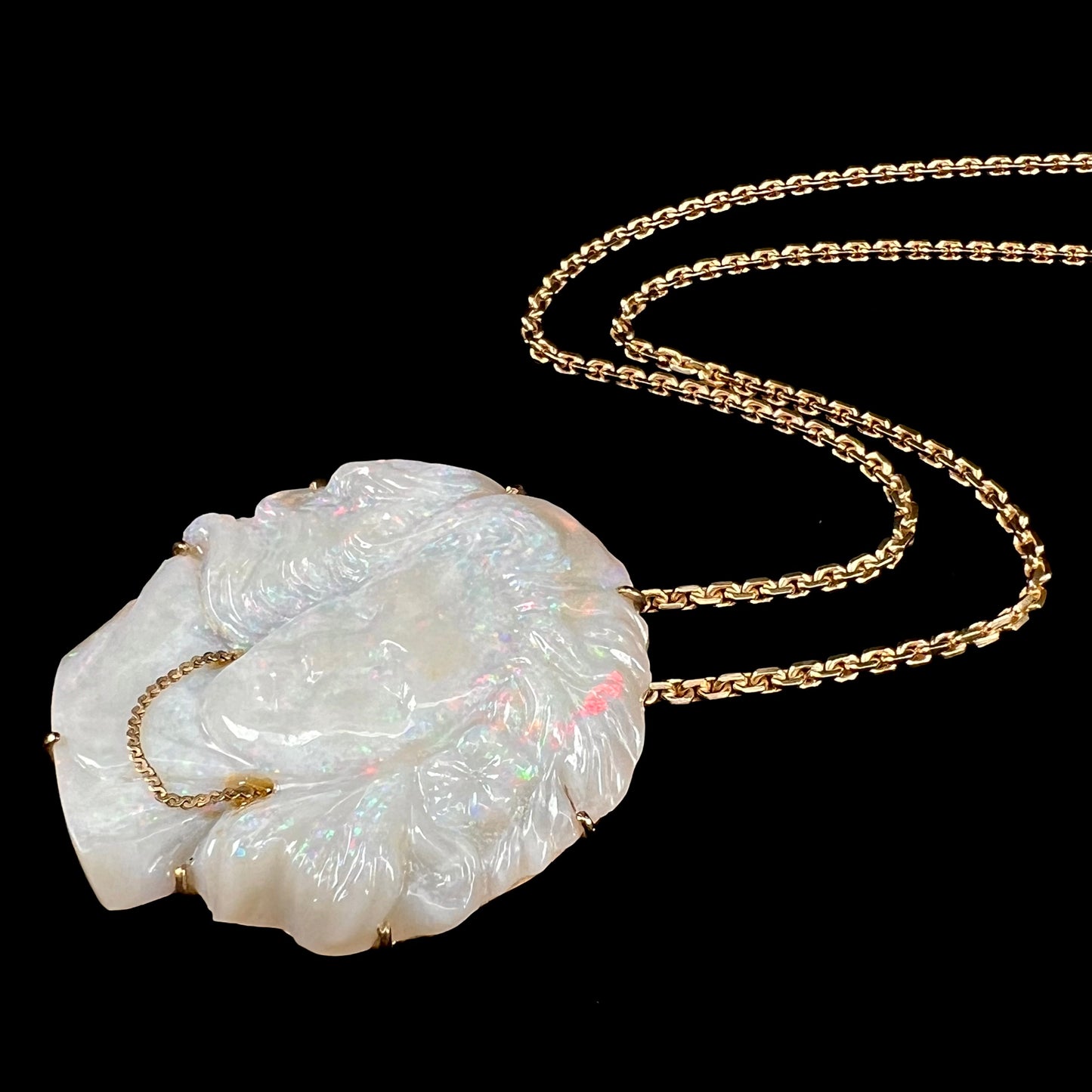 A cameo necklace carved by white crystal opal and held with gold prongs. The cameo is wearing a gold chain.