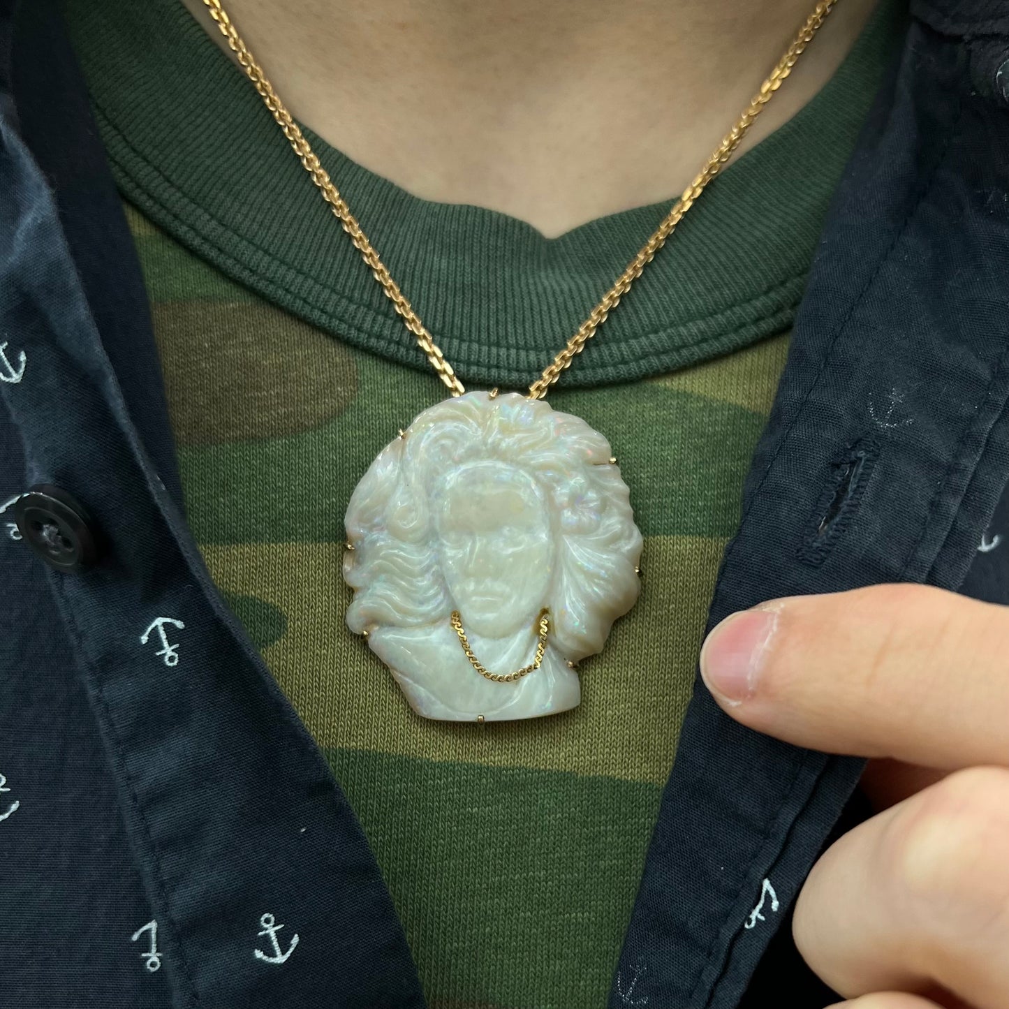 A cameo necklace carved by white crystal opal and held with gold prongs. The cameo is wearing a gold chain.