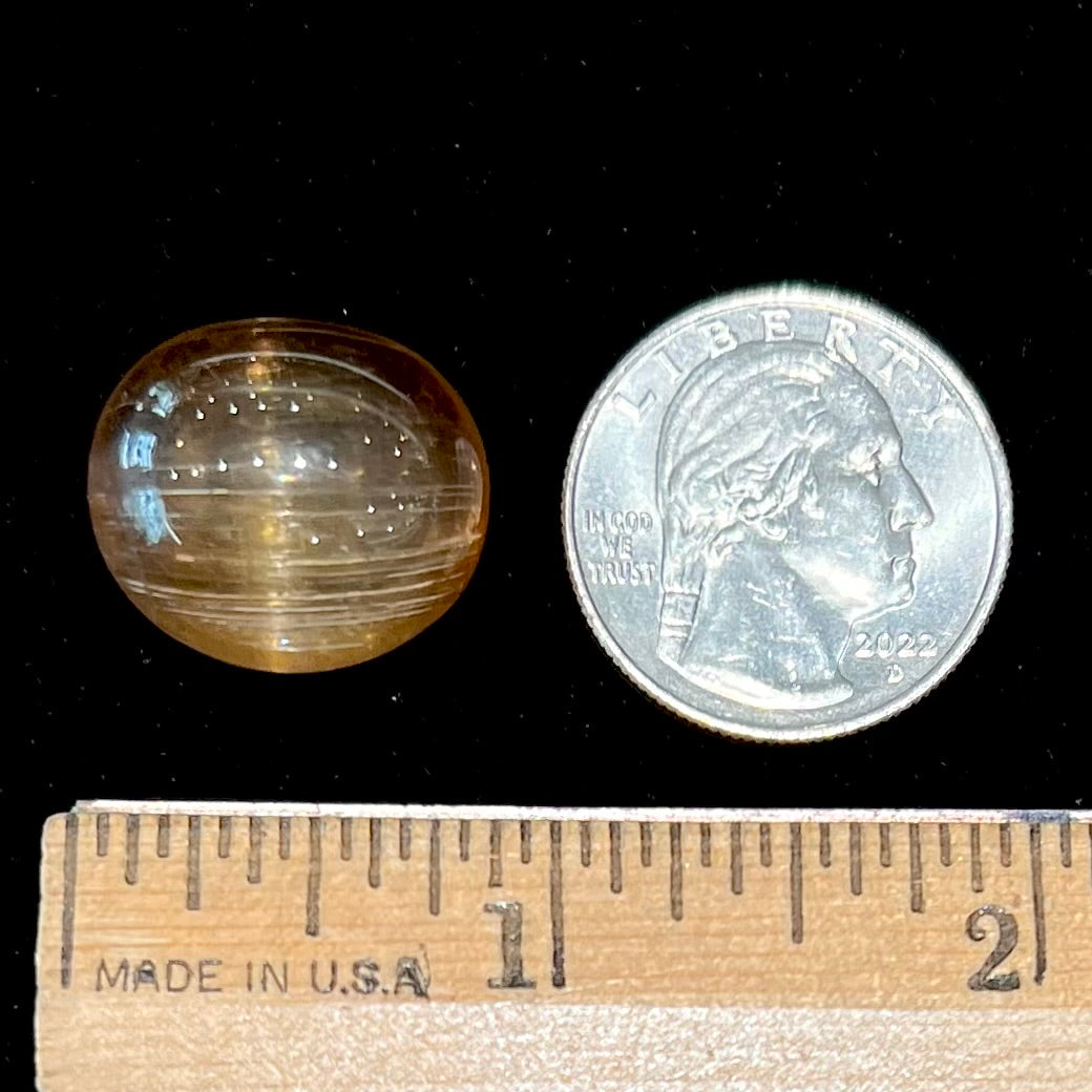 A loose, golden brown cat's eye dravite tourmaline gemstone. The stone is cut into an oval shaped cabochon.