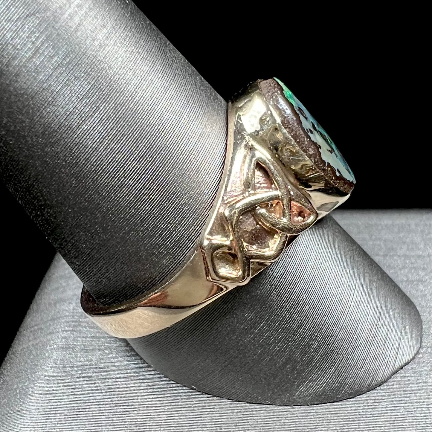 A unisex Celtic style natural boulder opal ring cast in yellow gold. The opal shines green and blue.