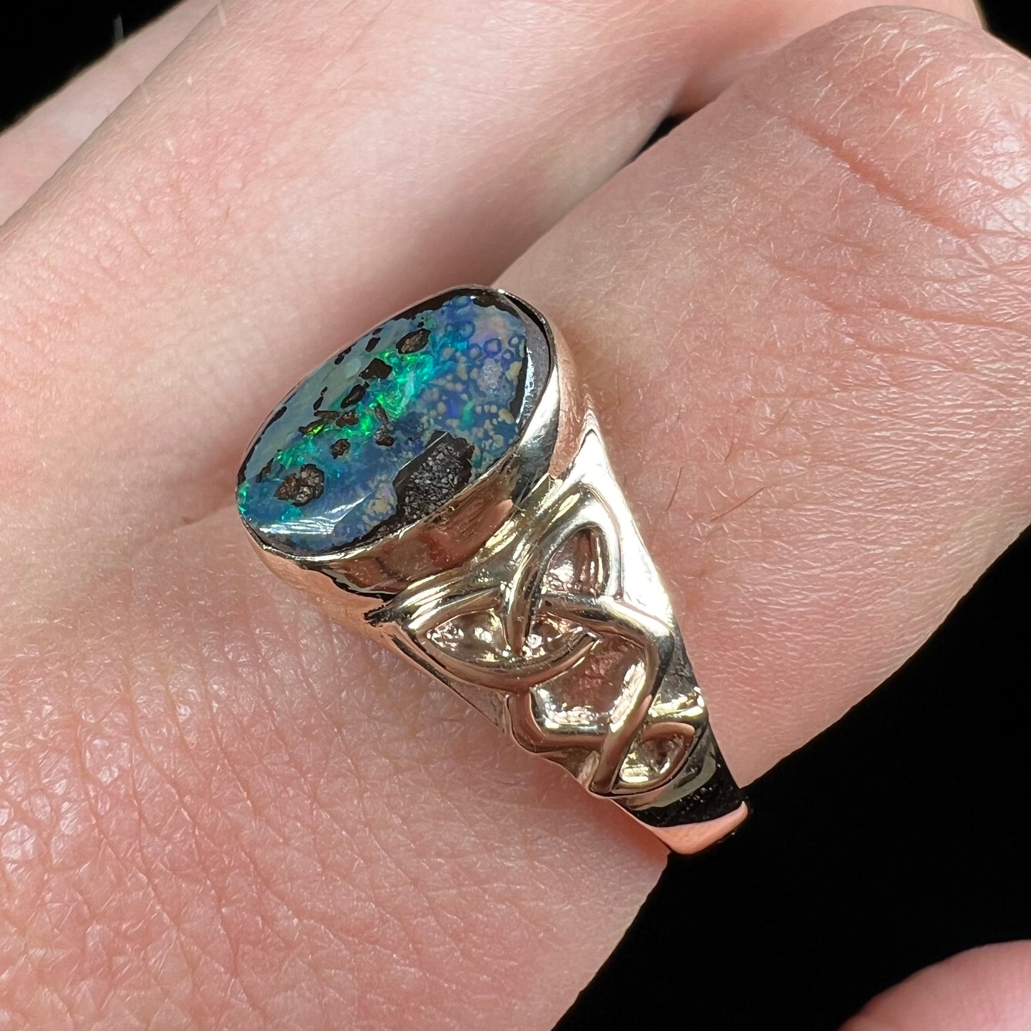 A unisex Celtic style natural boulder opal ring cast in yellow gold. The opal shines green and blue.