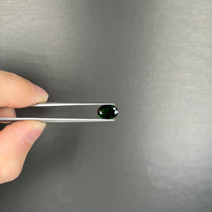 A faceted oval cut chrome tourmaline gemstone.  The stone is dark green.