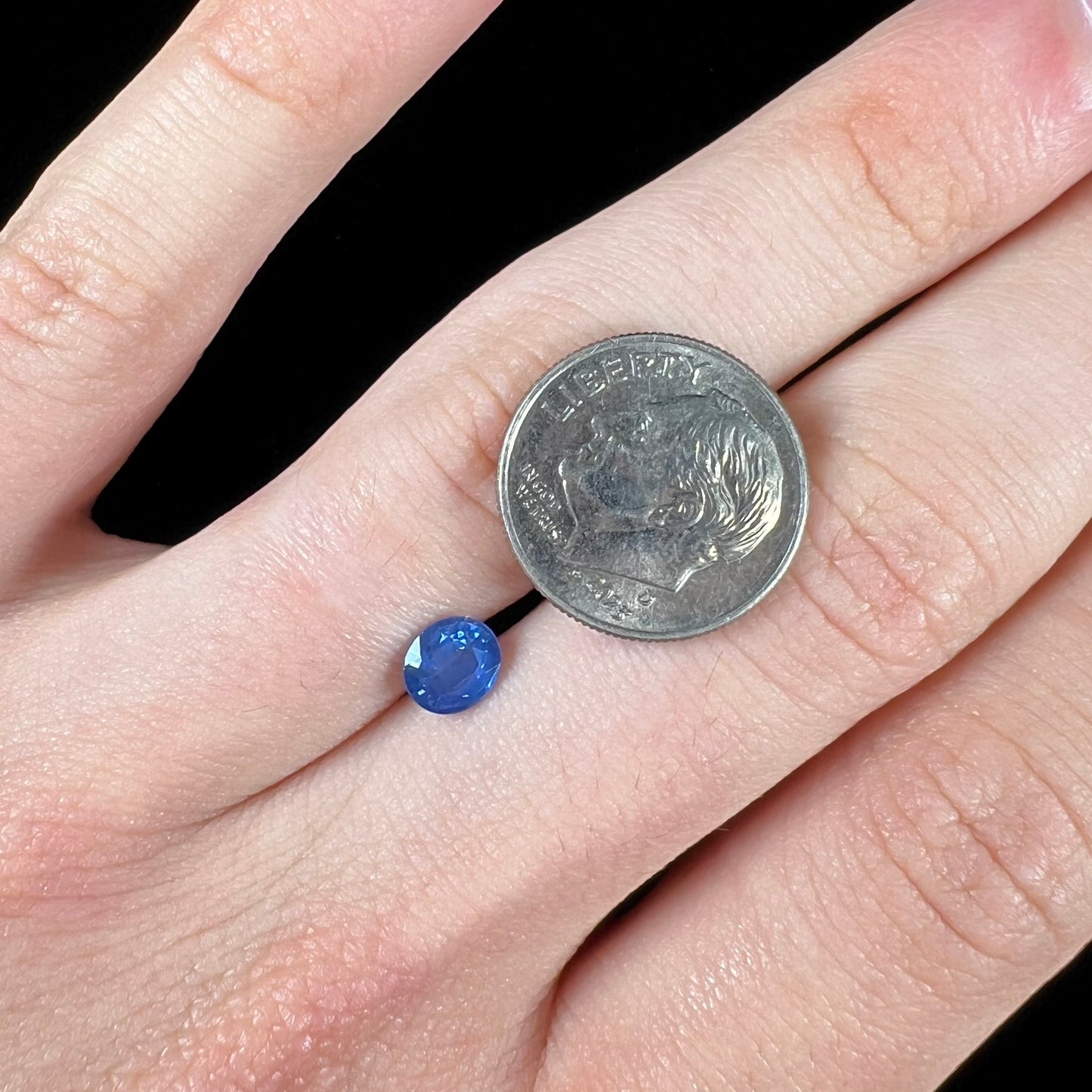 A loose, faceted oval cut natural blue sapphire. The color is a dark cornflower blue.