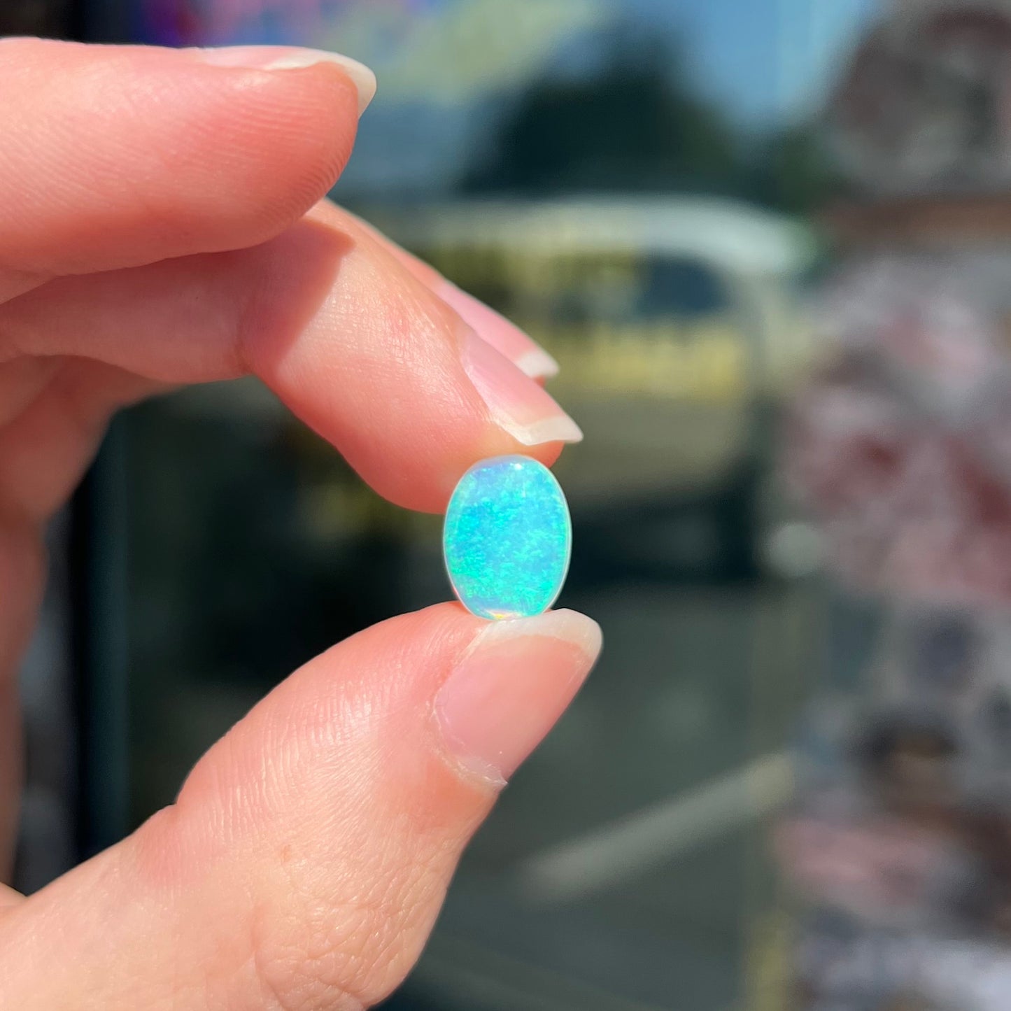 A loose, oval cabochon cut crystal opal from Coober Pedy, Australia. The opal has green and blue colors.