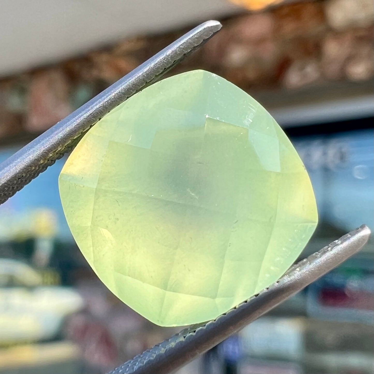 A loose, checkerboard cushion cut prehnite gemstone. The stone is a sleepy yellow green color.