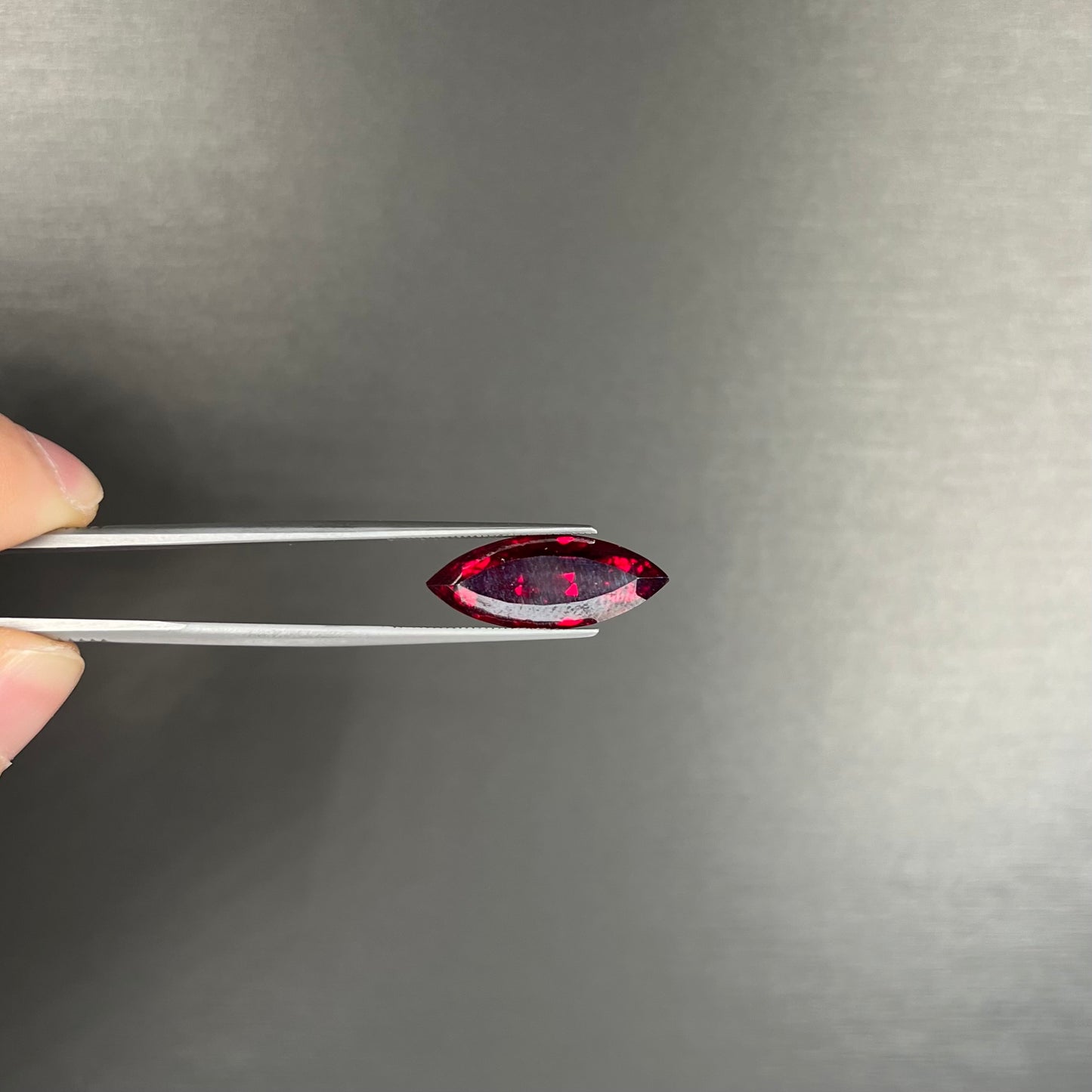 A loose, marquise cut cuprite gemstone. The stone is a deep, crimson red color.