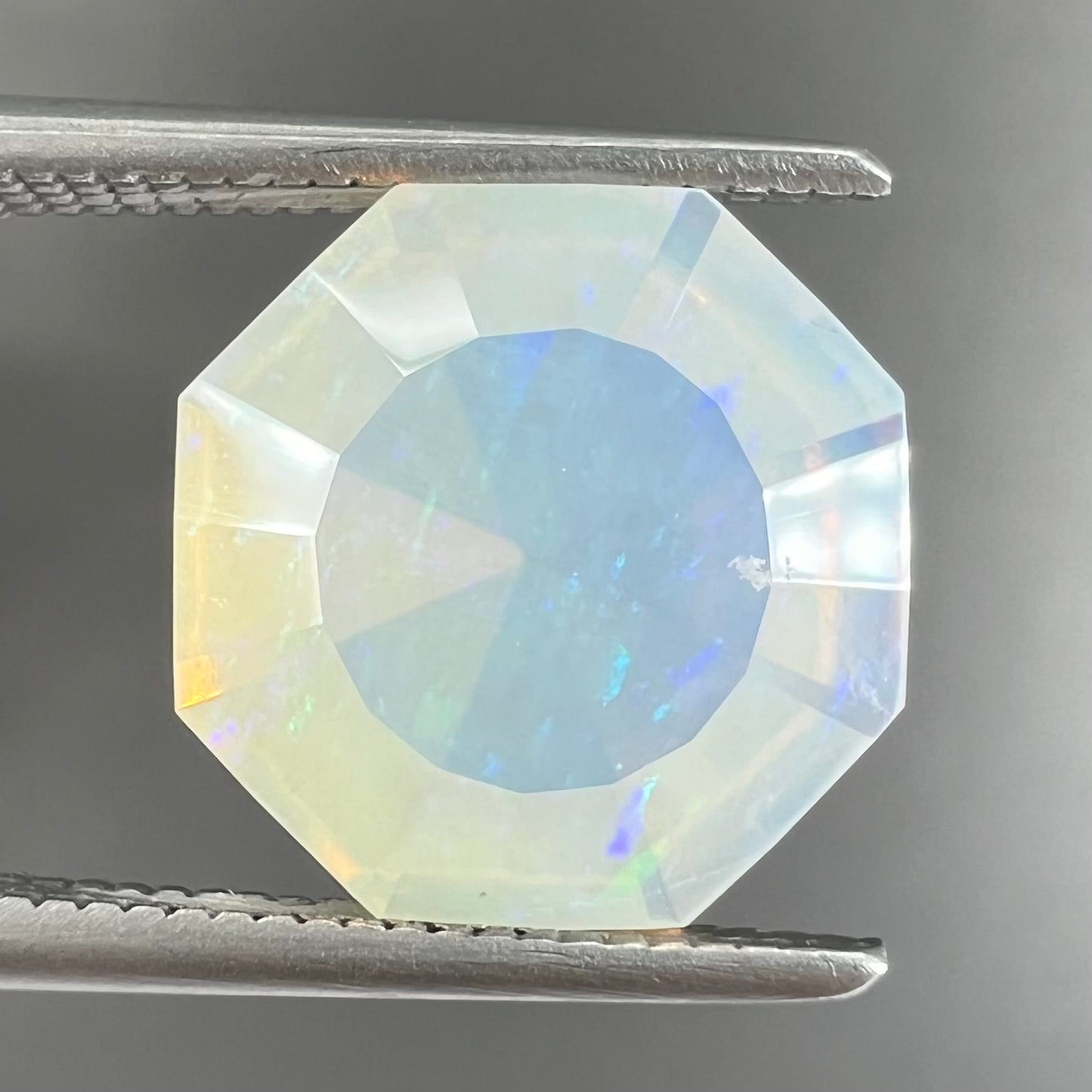 A loose, faceted octagon cut Mexican fire opal gemstone. The stone is a light yellow color with blue and green fire.