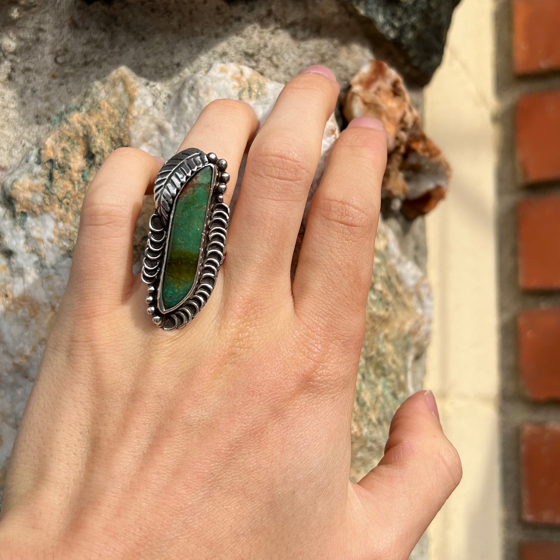 A sterling silver Navajo style ring set with a turquoise stone that shows colors of green, yellow, and reddish brown.