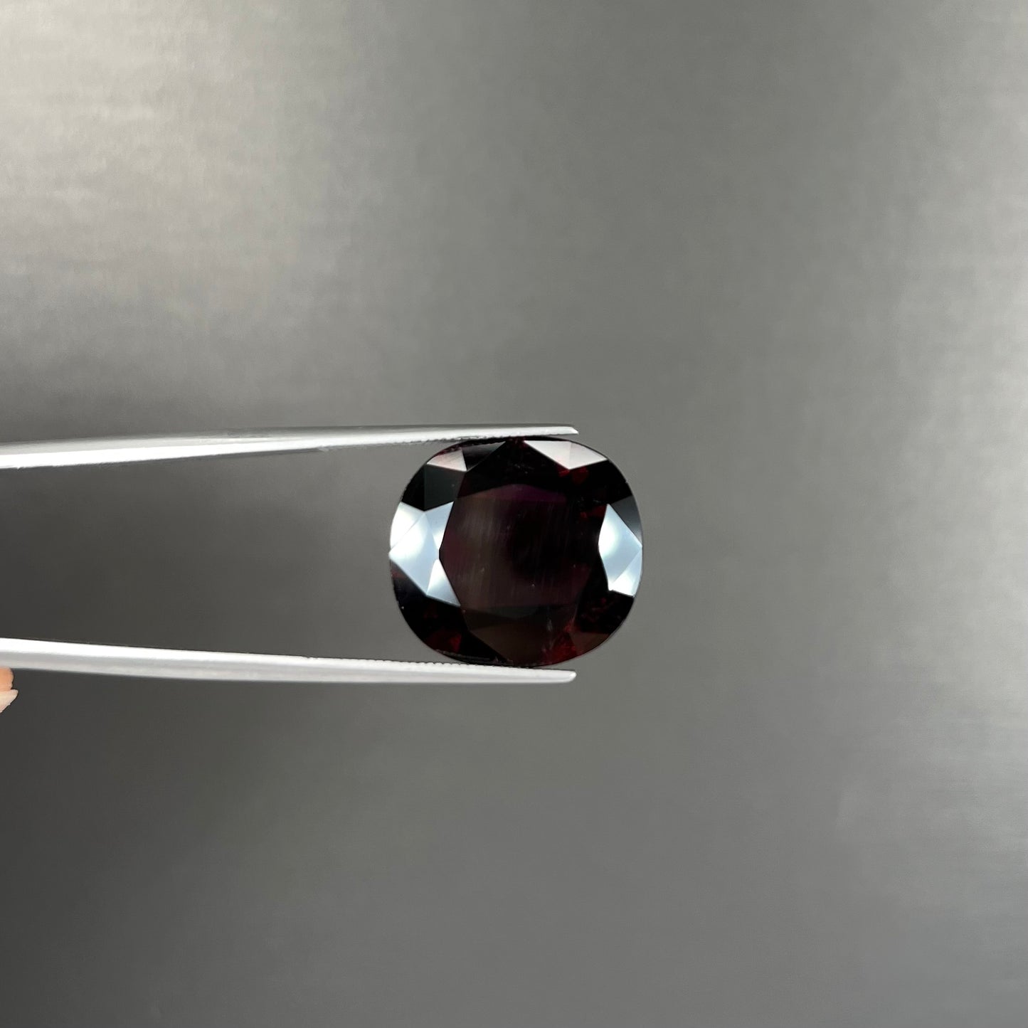 A loose, faceted oval cut rubellite tourmaline gemstone. The stone is a dark purple red color.
