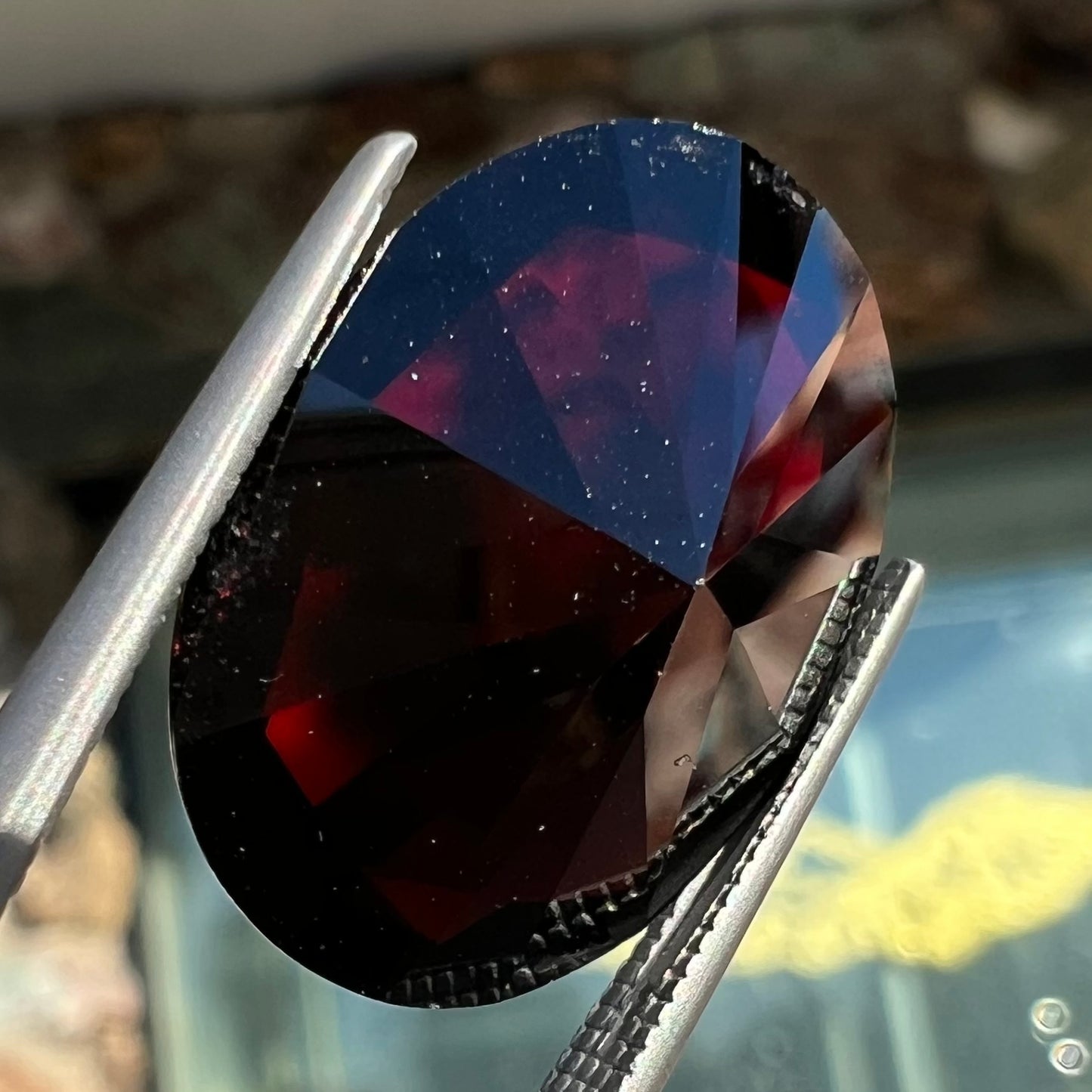 A loose, faceted oval cut pyrope garnet gemstone. The stone is a deep, dark red color.