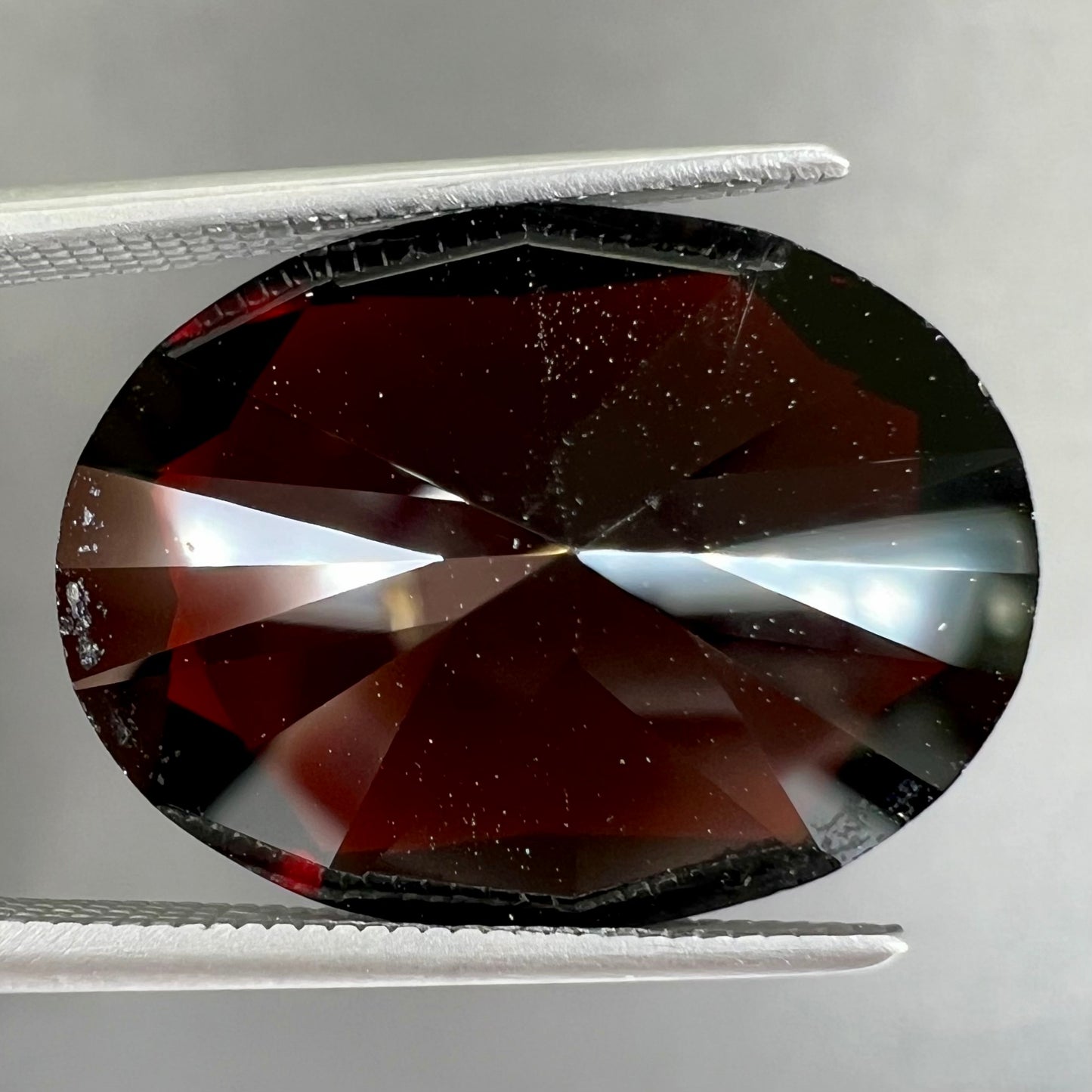 A loose, faceted oval cut pyrope garnet gemstone. The stone is a deep, dark red color.