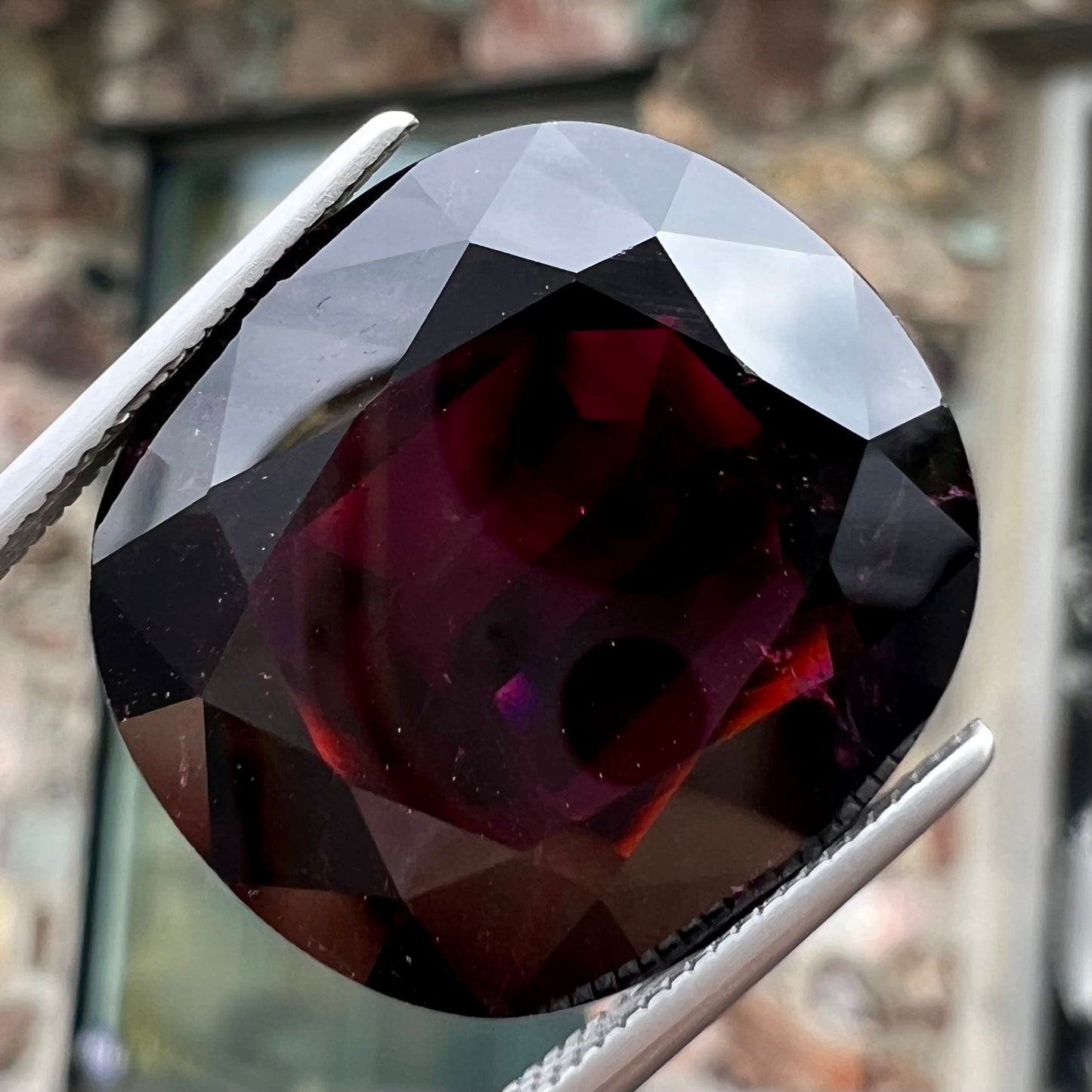 A loose, faceted oval cut rubellite tourmaline gemstone. The stone is a dark purple red color.