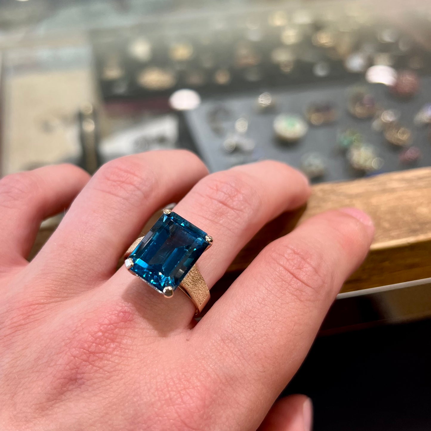 A ladies' yellow gold London blue topaz solitaire ring. The ring is textured, and the topaz is emerald cut.