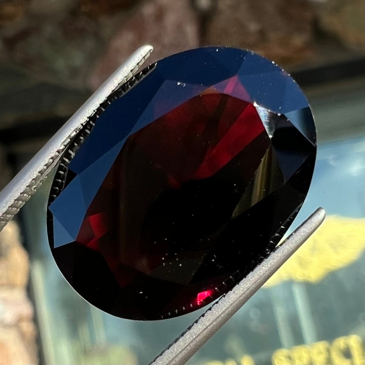 A loose, faceted oval cut pyrope garnet gemstone. The stone is a deep, dark red color.
