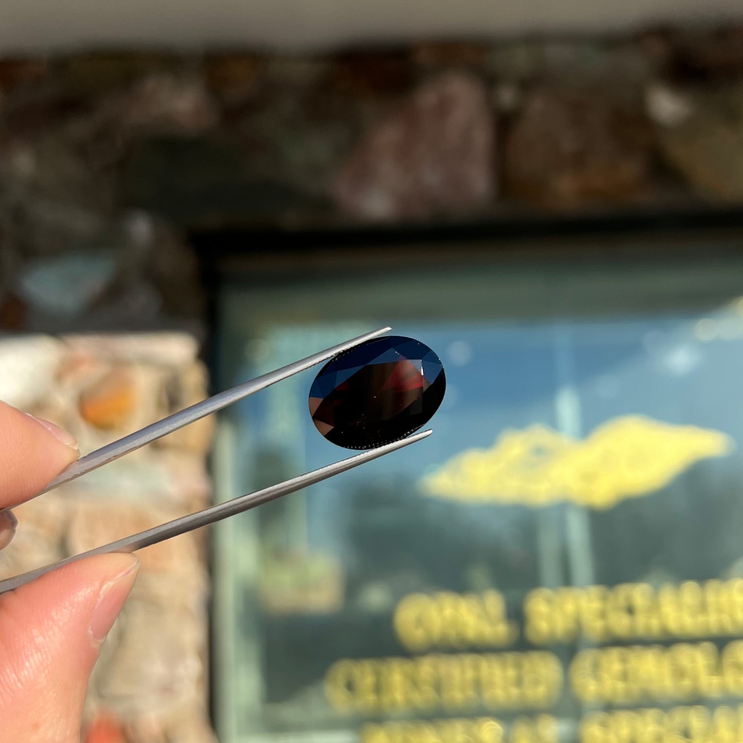 A loose, faceted oval cut pyrope garnet gemstone. The stone is a deep, dark red color.