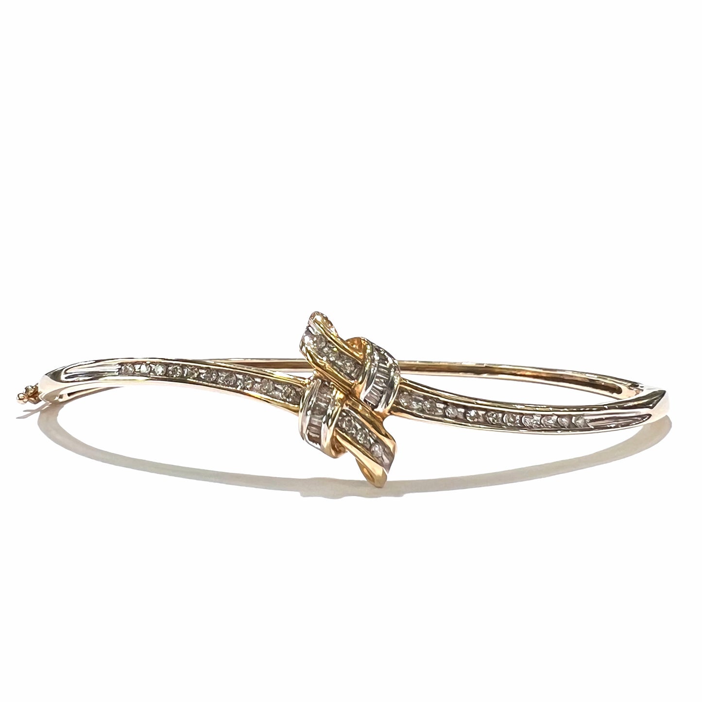 A ladies' knot style yellow gold bangle bracelet set with round and baguette cut diamonds.