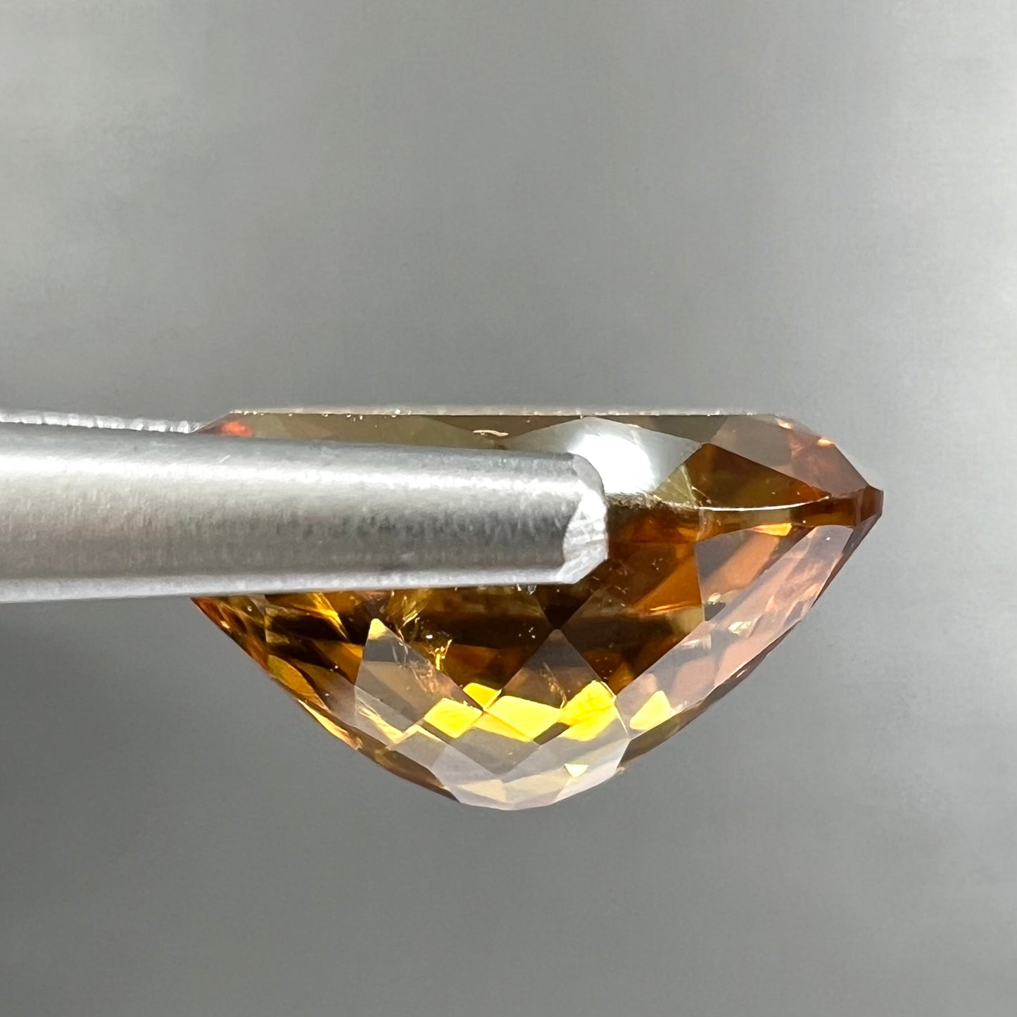 A loose, faceted oval cut orange dravite tourmaline gemstone.