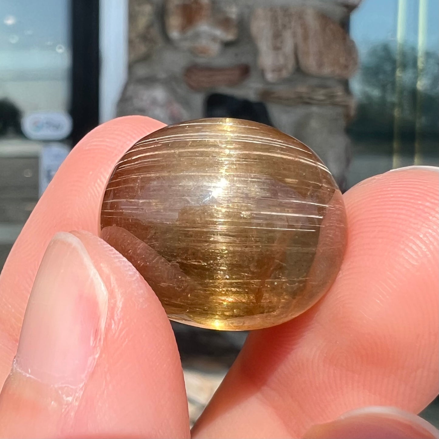 A loose, golden brown cat's eye dravite tourmaline gemstone. The stone is cut into an oval shaped cabochon.