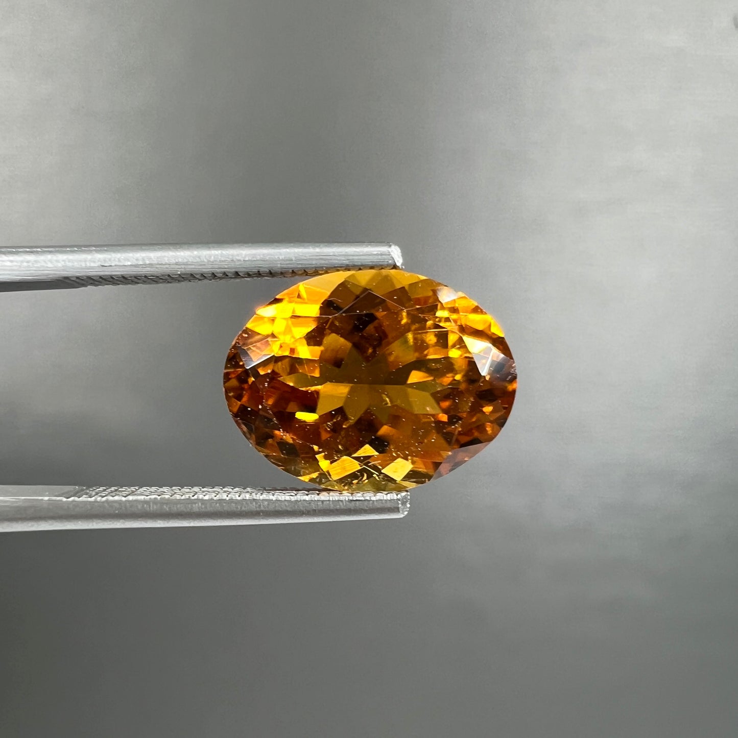 A loose, faceted oval cut orange dravite tourmaline gemstone.