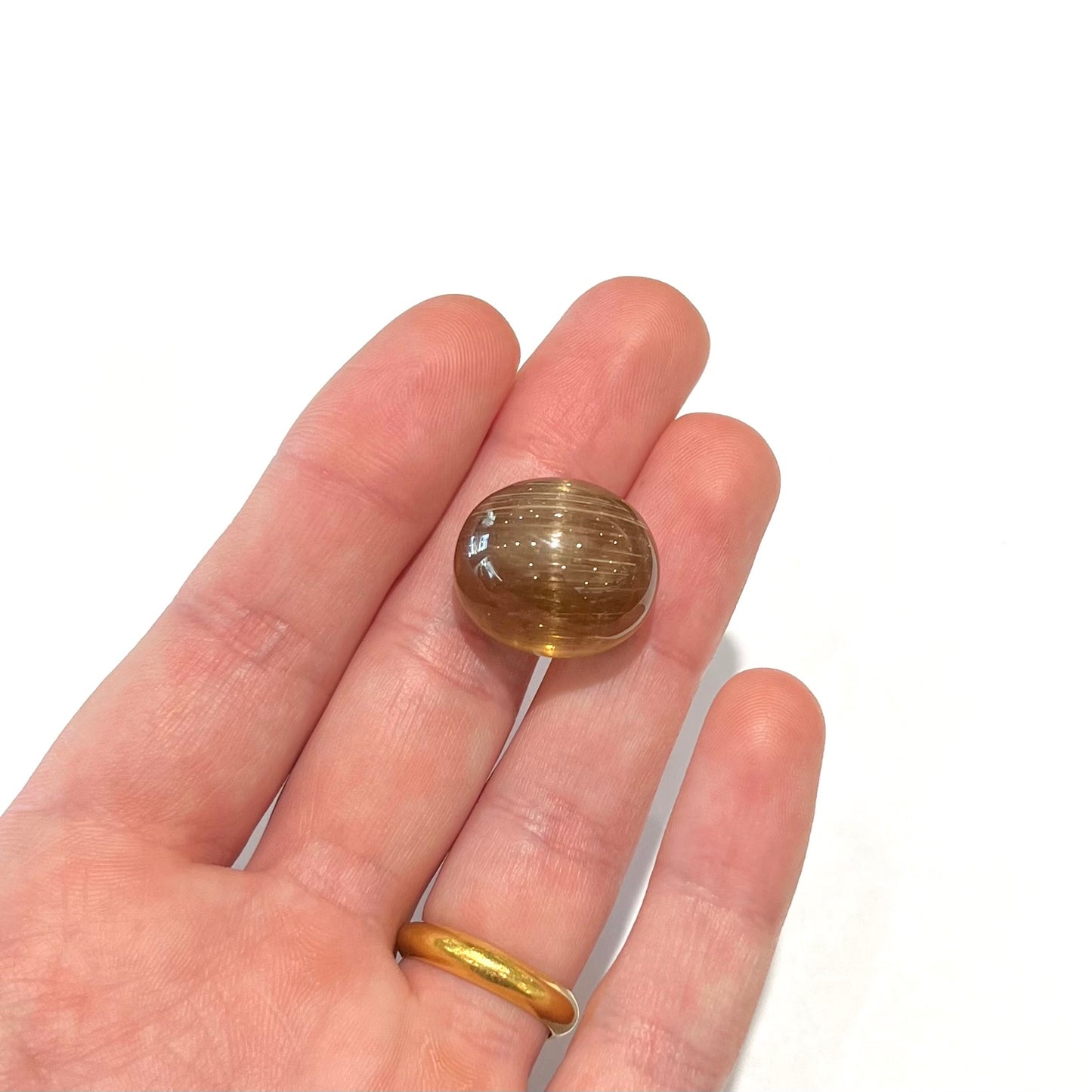 A loose, golden brown cat's eye dravite tourmaline gemstone. The stone is cut into an oval shaped cabochon.