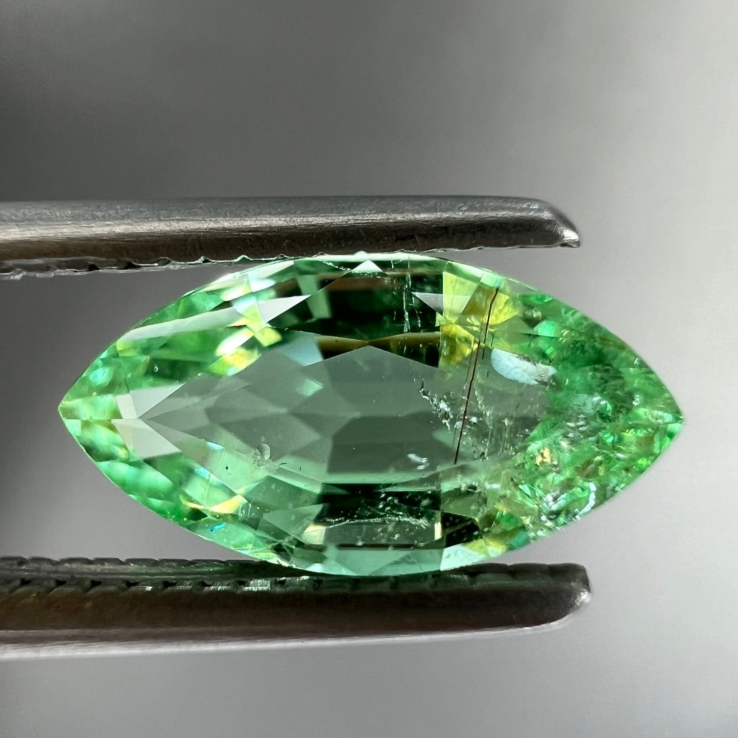 A faceted marquise cut electric green tourmaline gemstone. The stone has an eye-visible rutile needle inclusion.