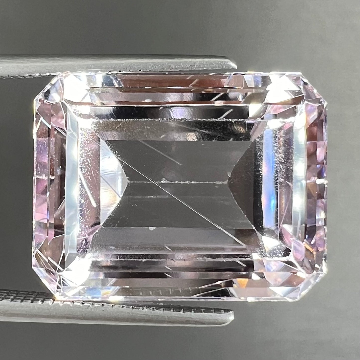 A loose, emerald cut kunzite gemstone. The stone has eye-visible rutile needle inclusions and the table is abraded.