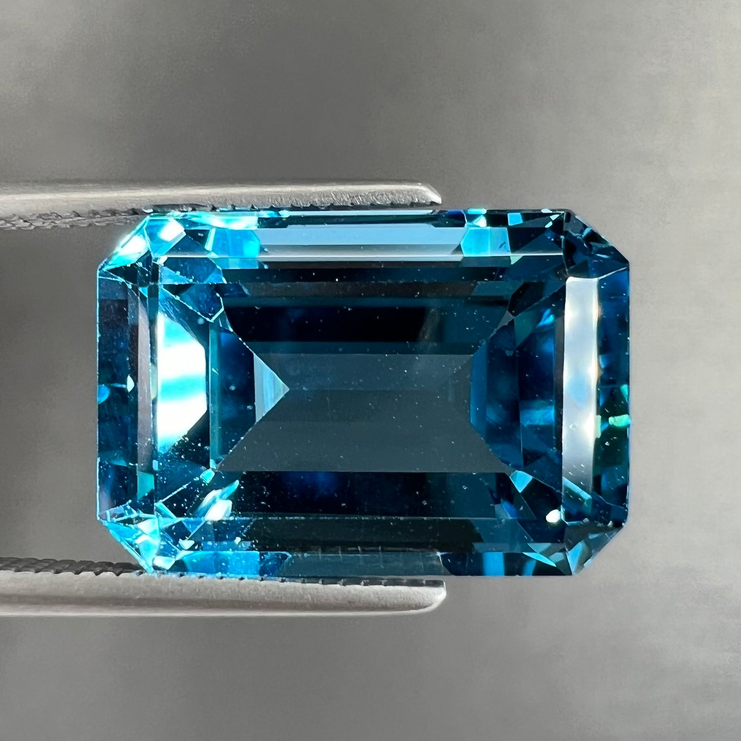 A loose, emerald cut London blue topaz gemstone. The stone is a deep, dark blue color.